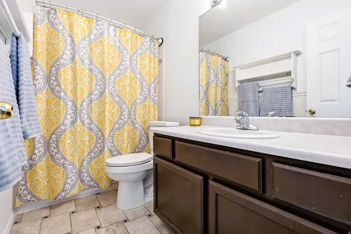 Primary Bathroom featuring a dark vanity with an integrated sink, a full-width mirror, and ceramic tile flooring