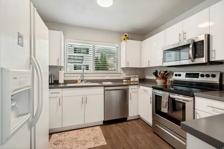 Modern kitchen featuring white cabinetry, dark countertops, stainless steel appliances, and wood-finish flooring