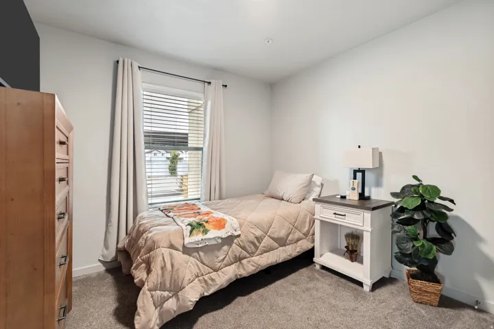 Carpeted room with a single window featuring horizontal blinds and light-colored drapes, complemented by white walls and a recessed ceiling light