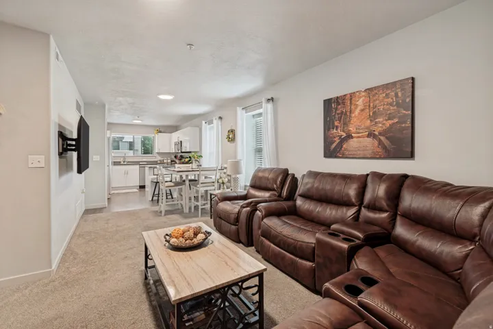Open-concept living area with neutral carpeting, recessed lighting, and a wall-mounted television bracket