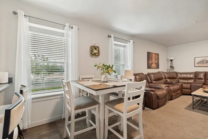 Open-concept living space featuring light neutral wall colors, a window with horizontal blinds, and a combination of carpet and wood-finish flooring