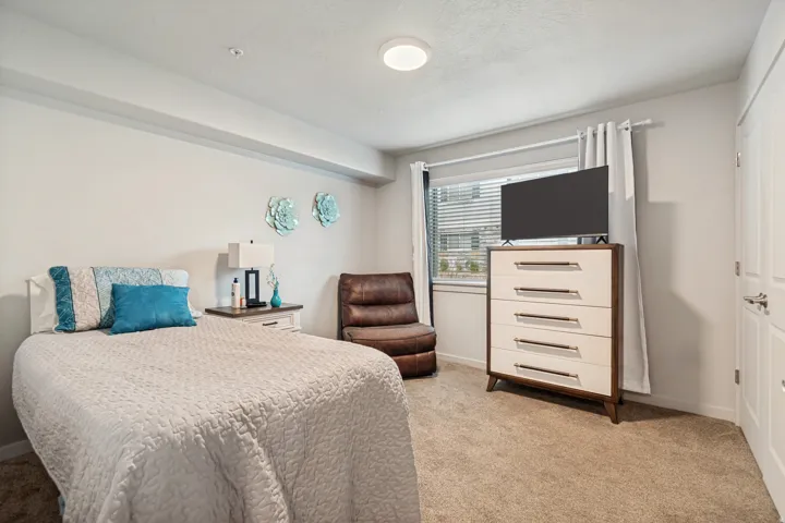 Carpeted room featuring a single window with blinds and drapes, light-colored walls, and a ceiling-mounted light fixture