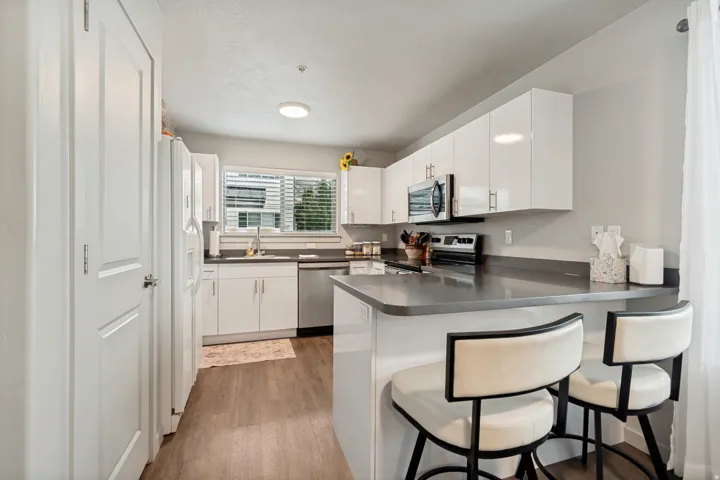 Bright kitchen featuring white cabinetry, wood-finish flooring, a stainless steel sink, a window with blinds, and a built-in kitchen island