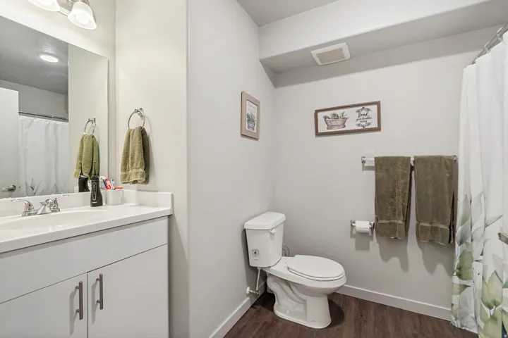 Bathroom featuring a single vanity with a white countertop and base cabinetry, a full-width mirror, and wood-finish flooring