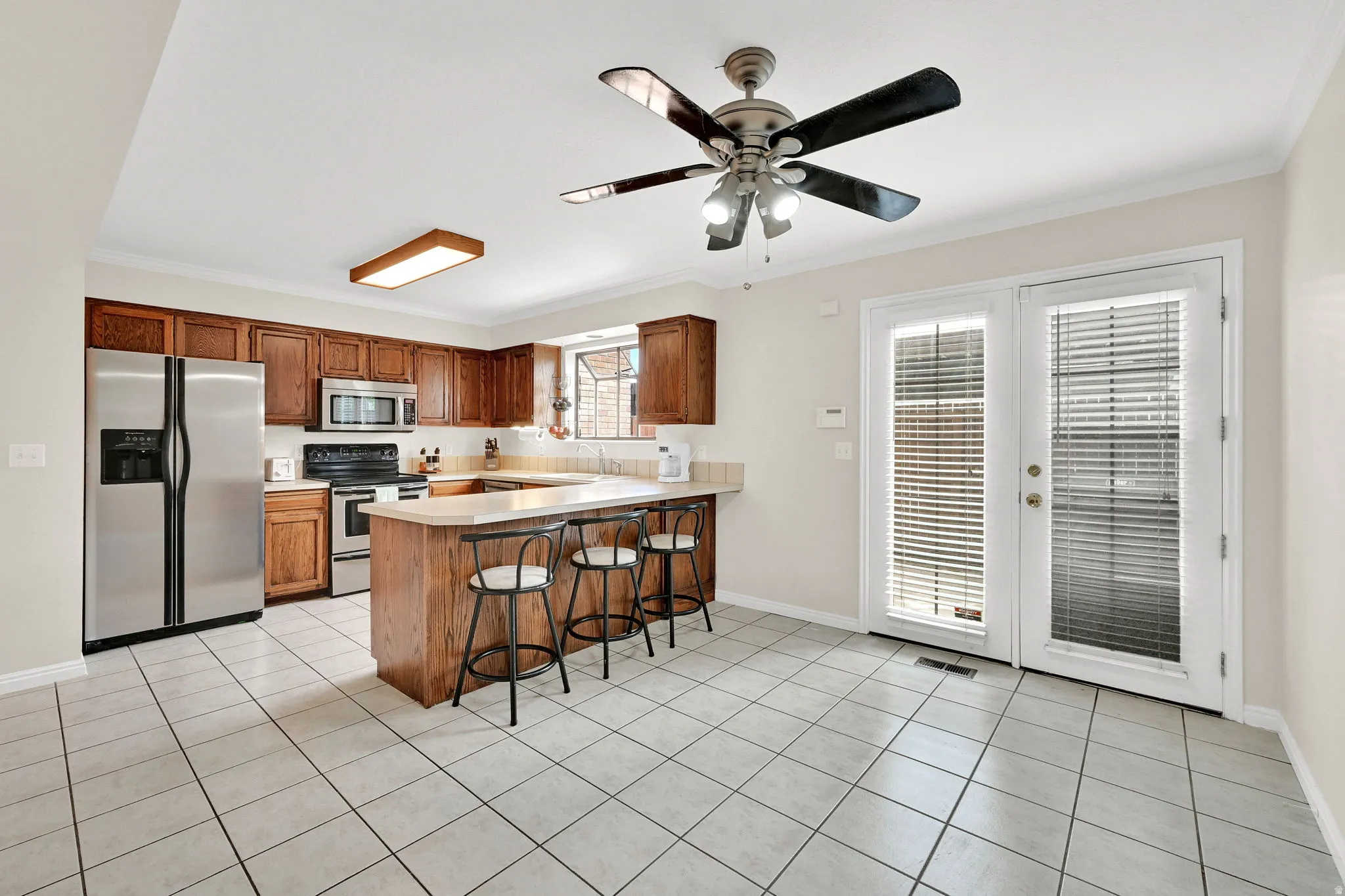 Kitchen featuring extensive wood cabinetry, stainless steel appliances, a breakfast bar, light-toned tile flooring, and French doors