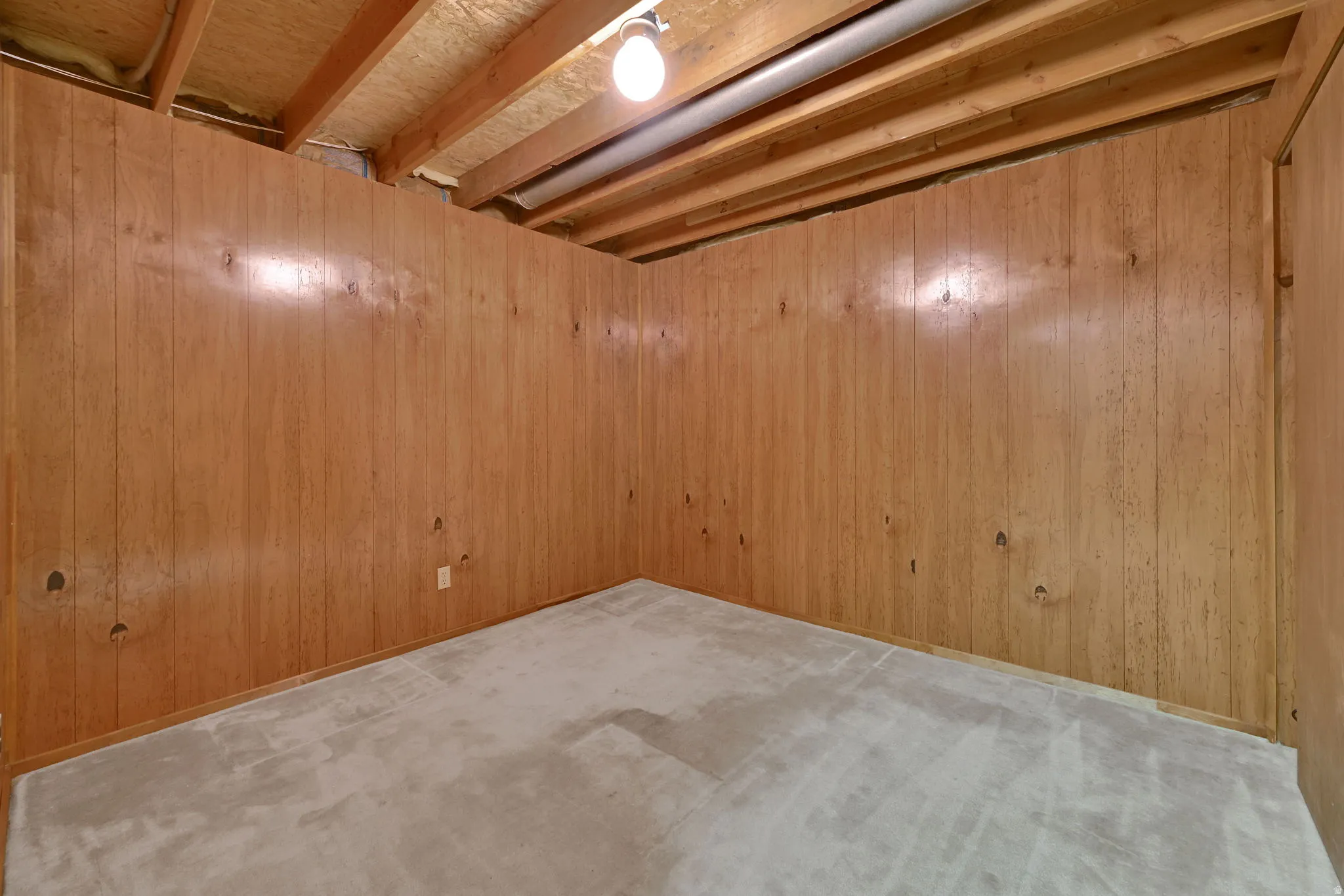Room with wood paneling, exposed ceiling joists, and a single ceiling-mounted light fixture