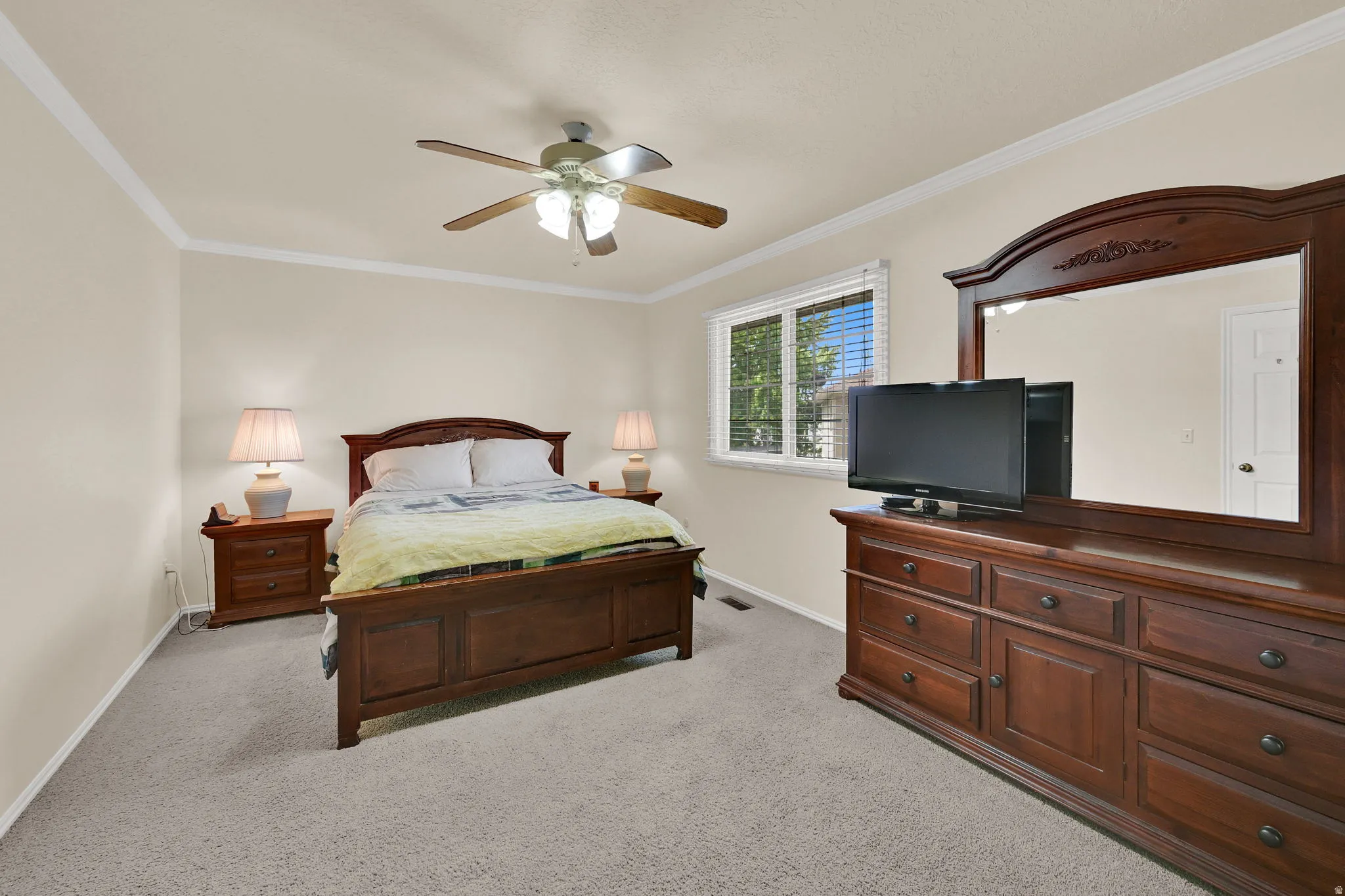 Carpeted bedroom featuring a ceiling fan with integrated lighting, a window with blinds, and white crown molding