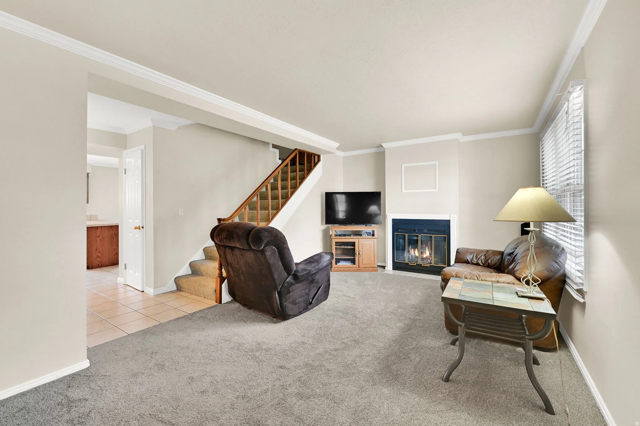 Living area featuring a fireplace with a dark metal insert, light-colored walls, crown molding, and gray carpeting