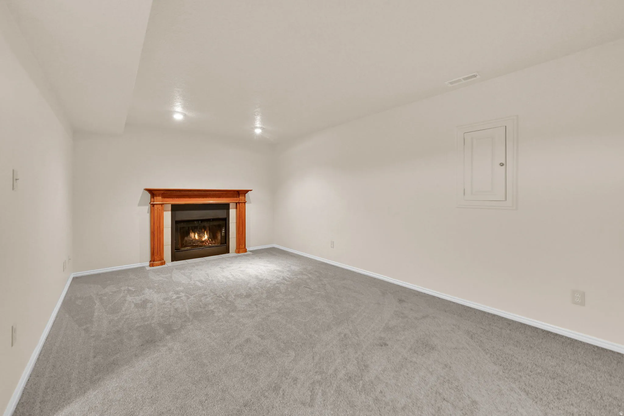 Spacious room featuring a fireplace with a wood-finish mantel and surround, light gray carpeting, neutral wall paint, and recessed ceiling lighting