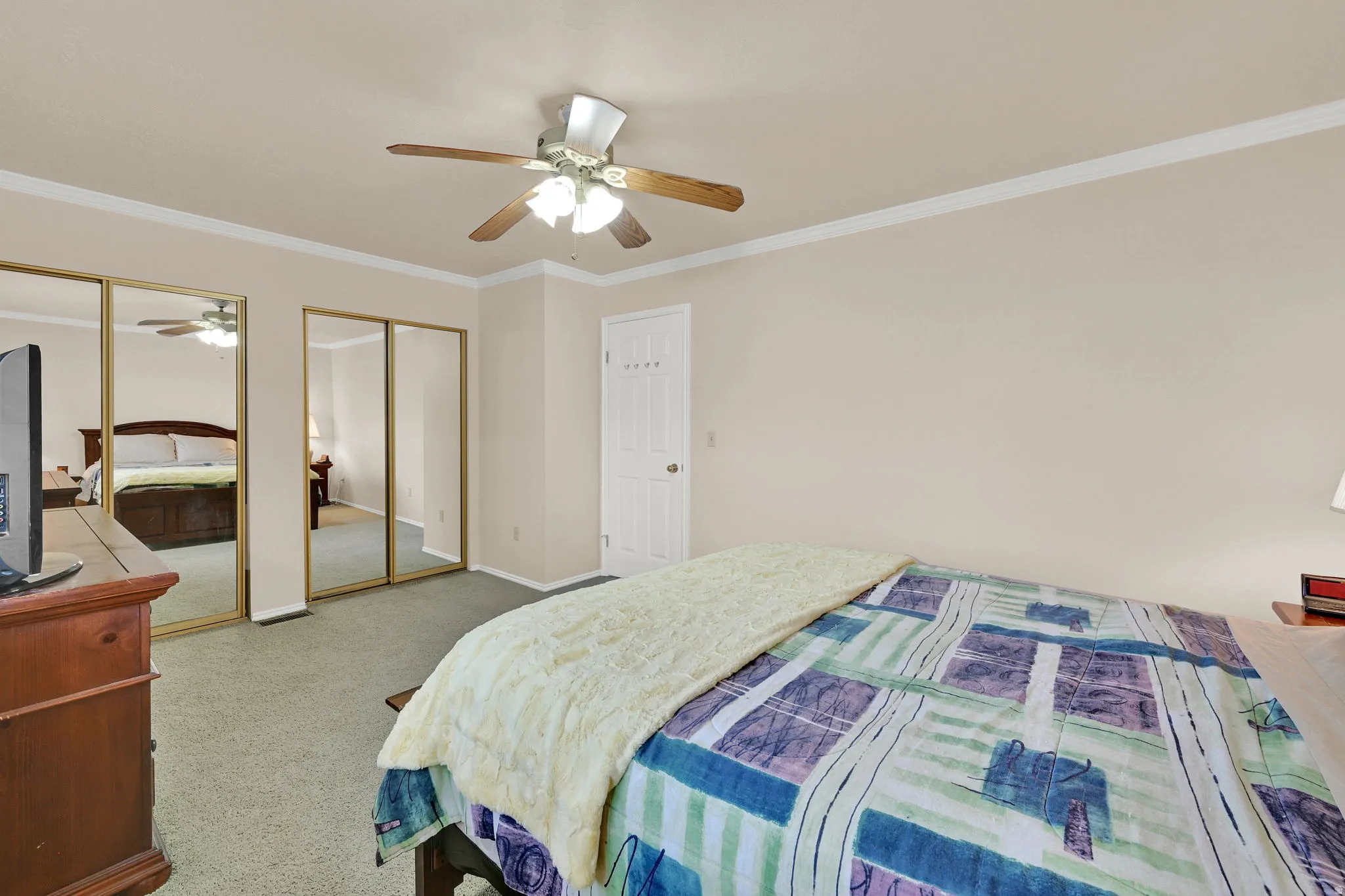 Bedroom featuring crown molding, neutral wall tones, carpet flooring, a ceiling fan with integrated lighting, and mirrored closet doors