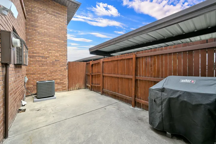 Private concrete patio featuring a perimeter wood fence, brick exterior, and a protective metal awning