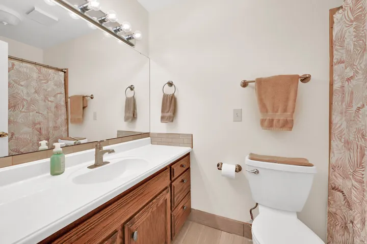 Bathroom vanity featuring a white countertop with integrated sink, brushed nickel faucet, wood-finish cabinetry, and a full-width mirror with a five-bulb vanity light fixture