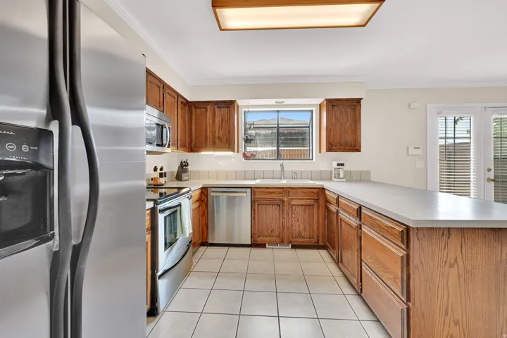 U-shaped kitchen featuring wood cabinetry, stainless steel appliances, white tile flooring, and a large countertop peninsula