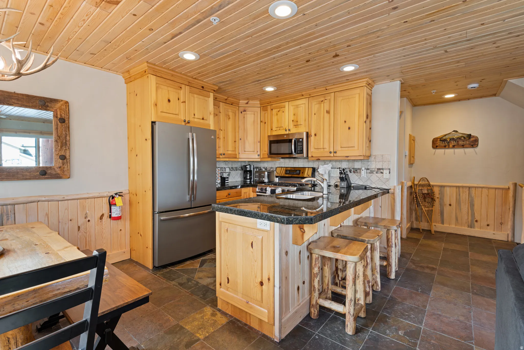 Kitchen featuring a natural wood plank ceiling, slate tile flooring, stainless steel appliances, wood cabinetry, and a granite-topped island with seating