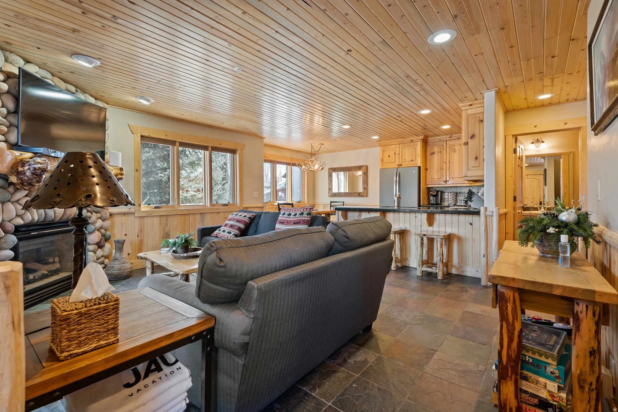 Open concept living area featuring a stone-clad fireplace, wood-finish flooring, and natural wood paneling