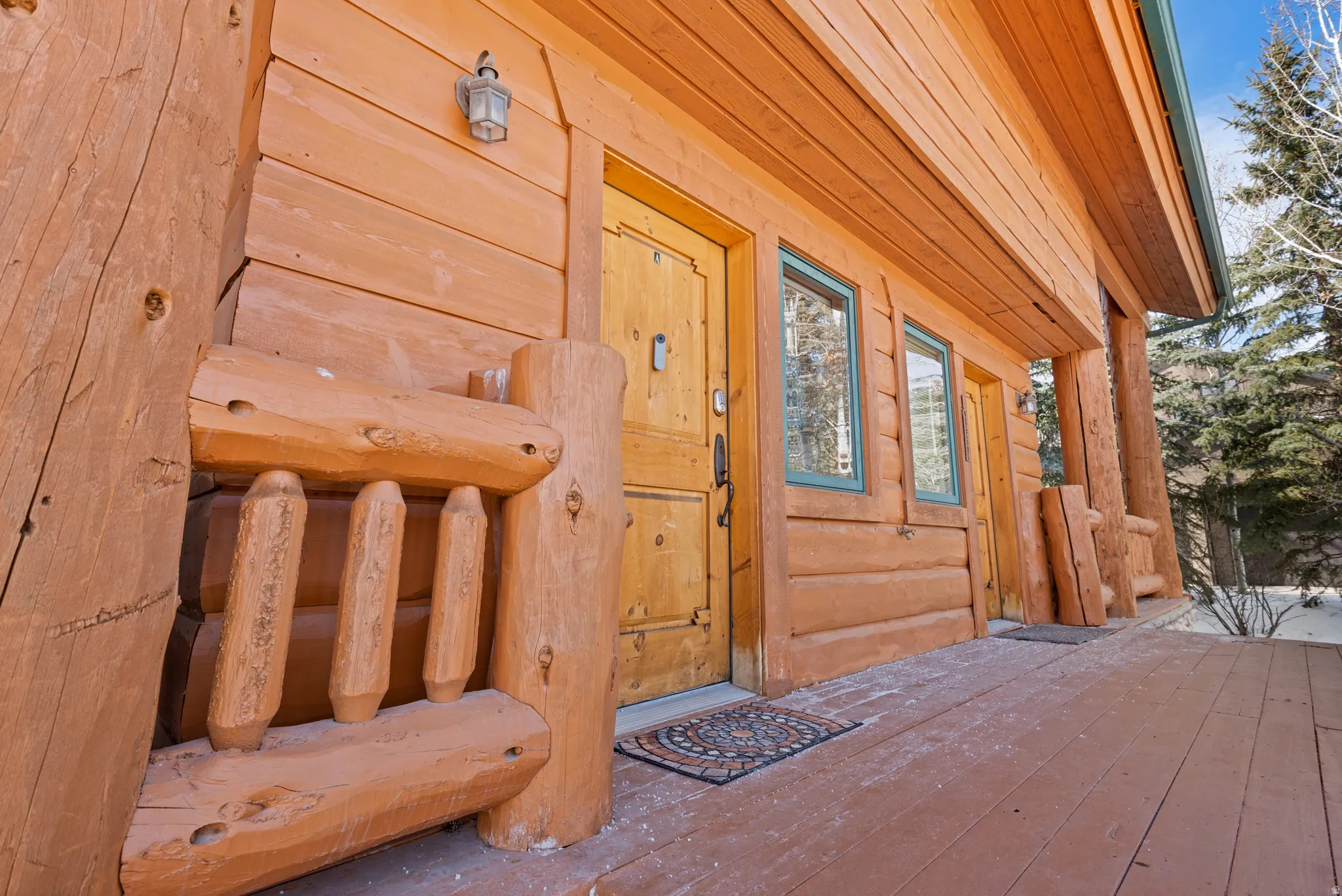 Log cabin exterior featuring a natural wood-finish door, rustic outdoor lighting, two framed windows, and a wood-finish porch