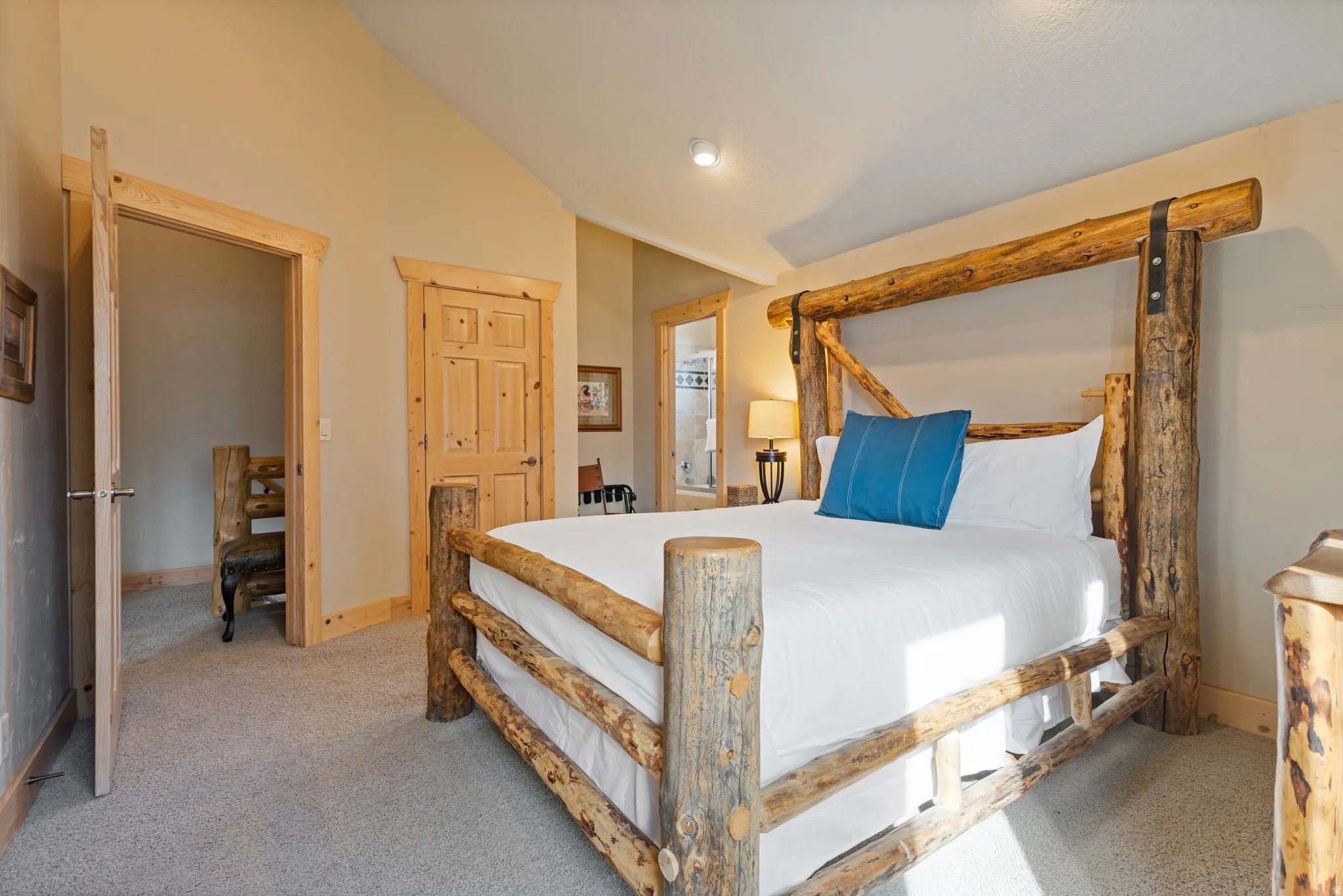 Spacious room featuring vaulted ceilings, light-toned carpeting, and natural wood trim around doors