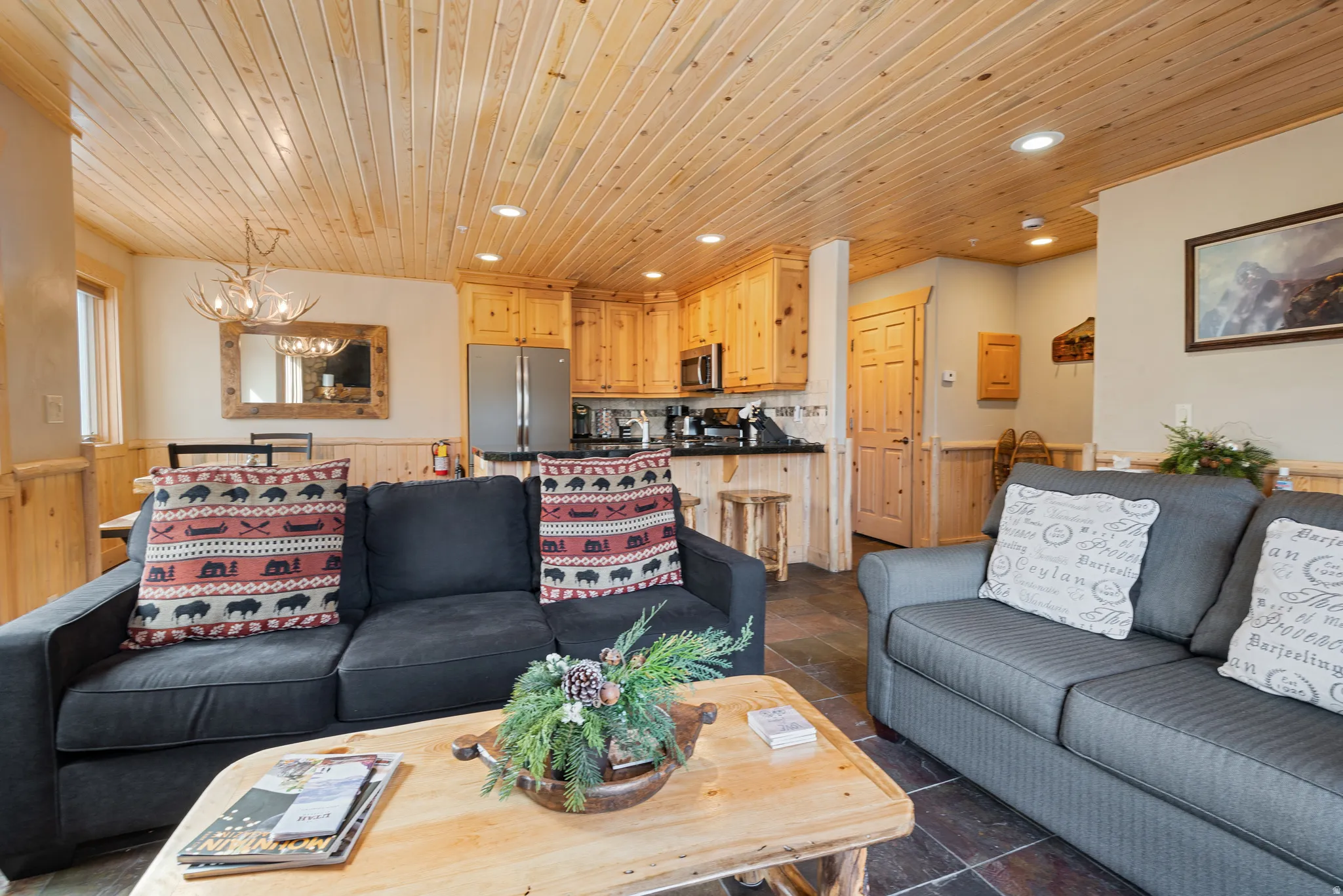 Open-concept living space featuring wood-paneled ceilings, wood-finish flooring, and a kitchen with wood cabinetry and stainless steel appliances