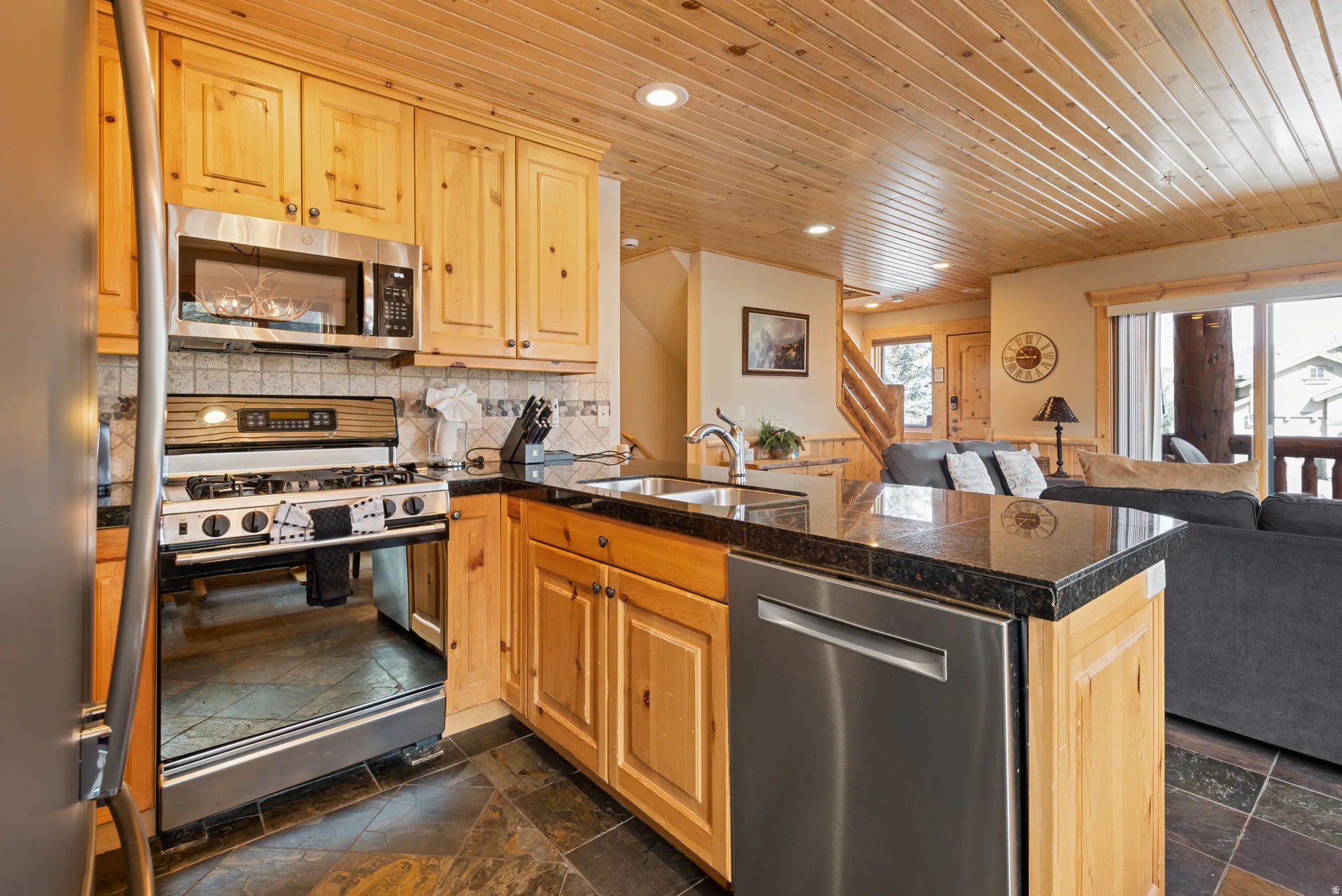 Kitchen featuring wood cabinetry, stainless steel appliances, dark stone countertops, and a tile backsplash