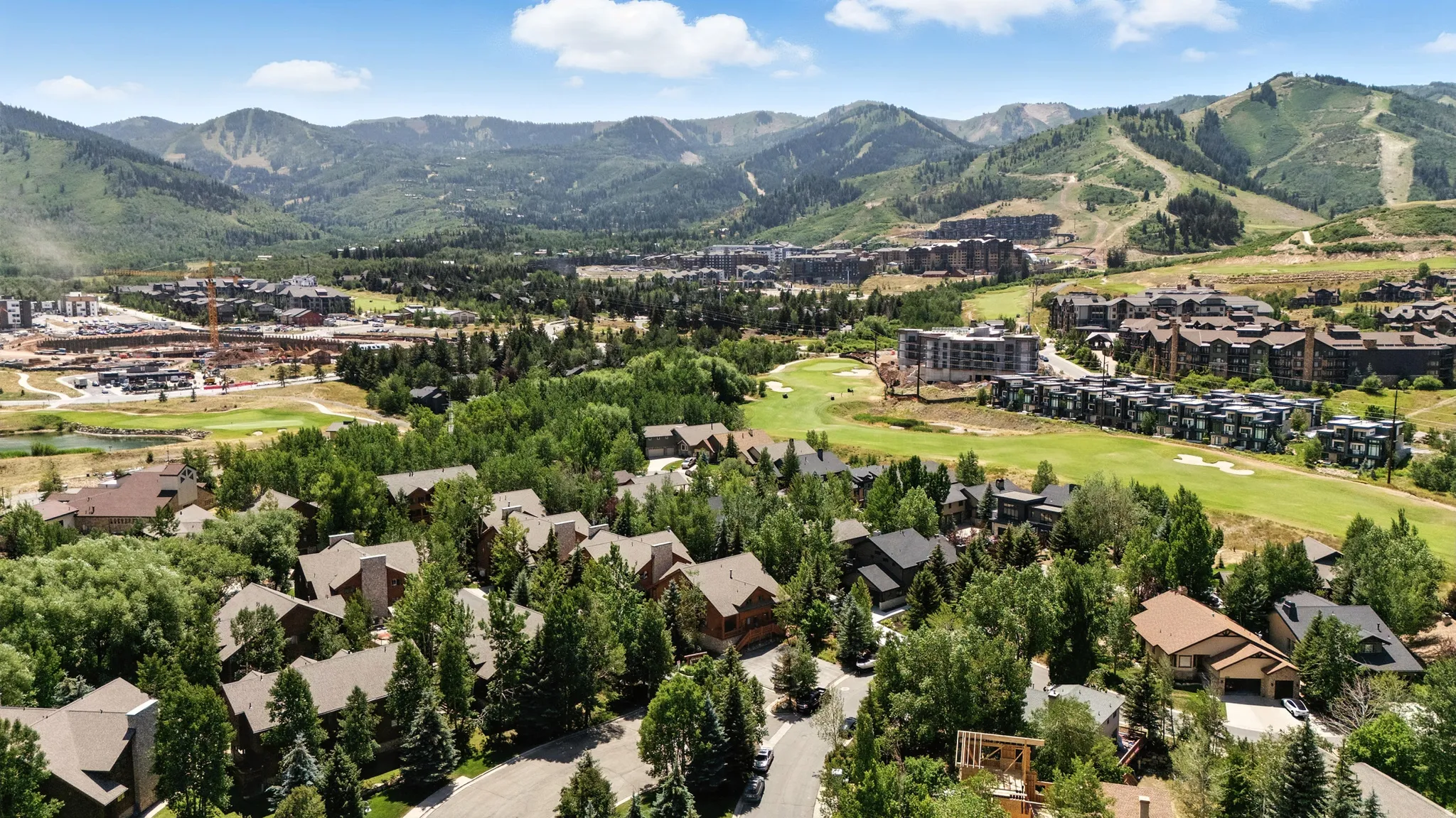 Expansive aerial showcasing a residential community amidst a mountainous landscape with abundant mature trees