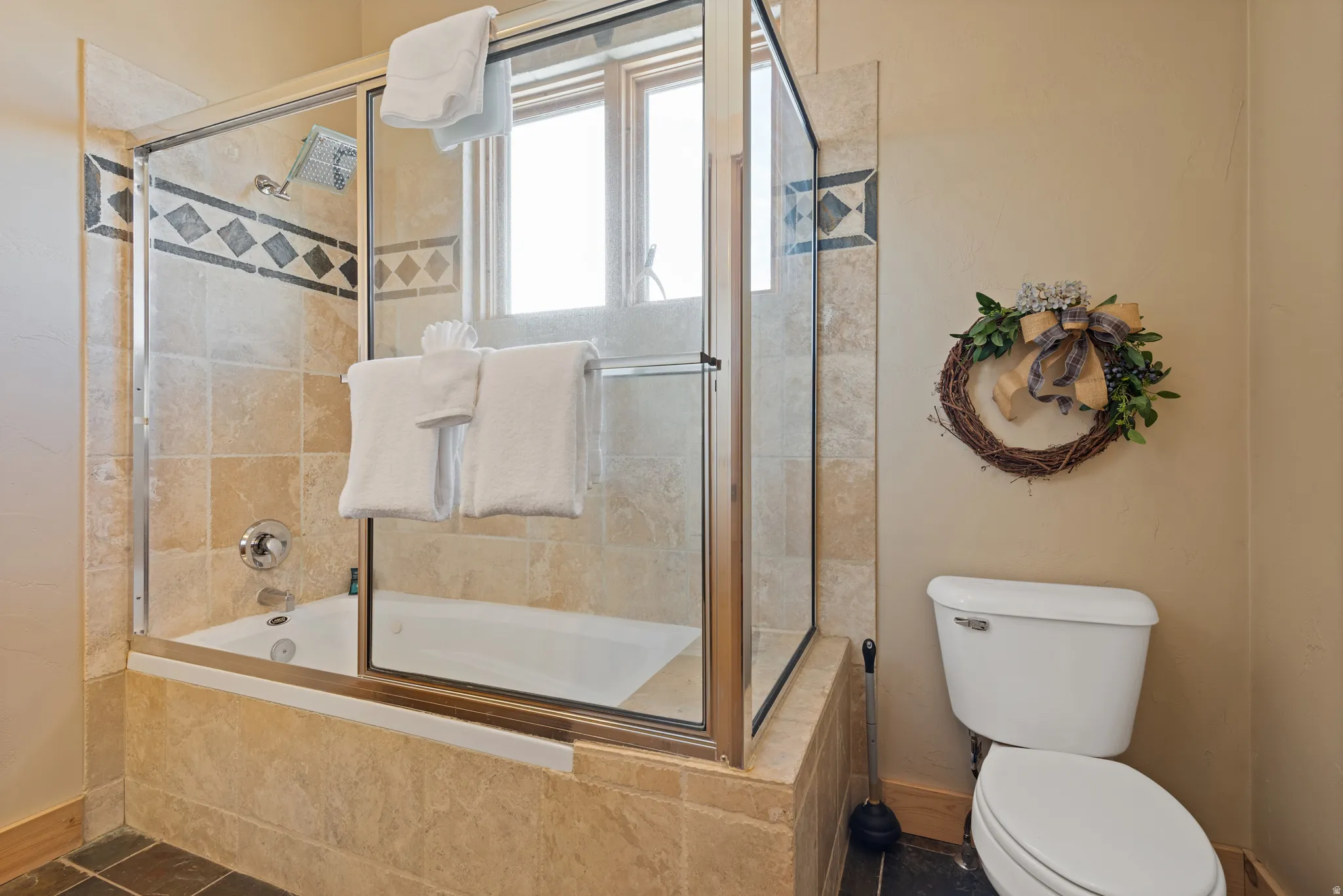 Bathtub with full tile surround, featuring a decorative tile band and glass shower enclosure
