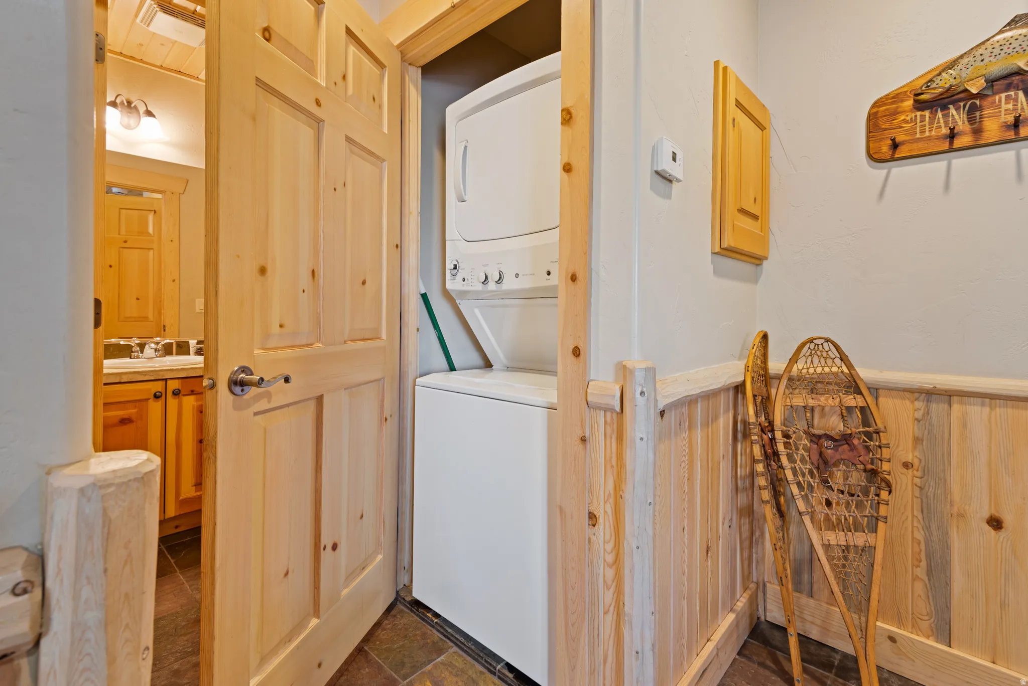 Dedicated laundry closet with stacked washer and dryer, featuring wood-paneled walls and durable tile flooring