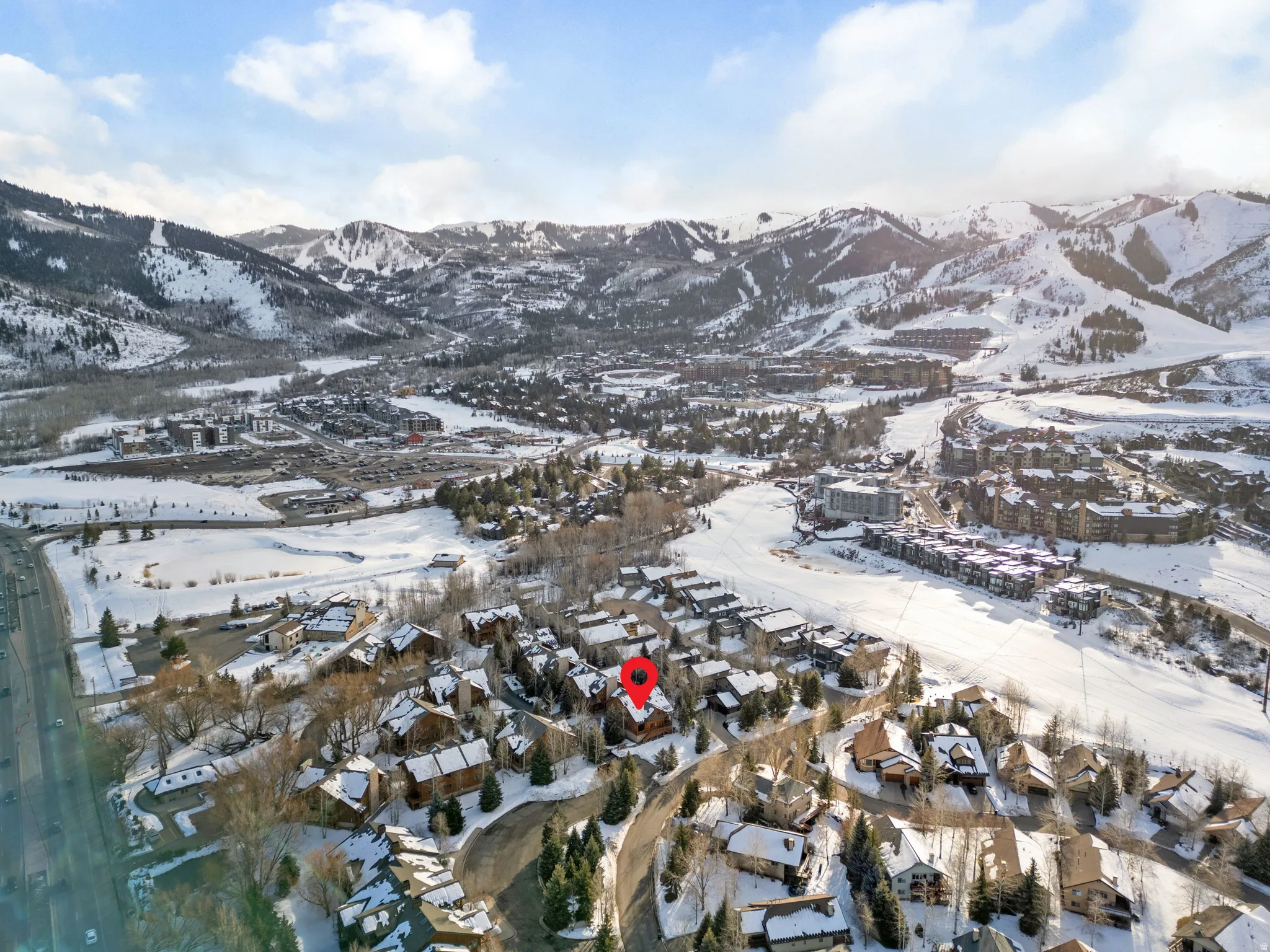 Aerial perspective showcasing the property surrounded by snow-covered trees and residential structures, set against a backdrop of snow-capped mountains