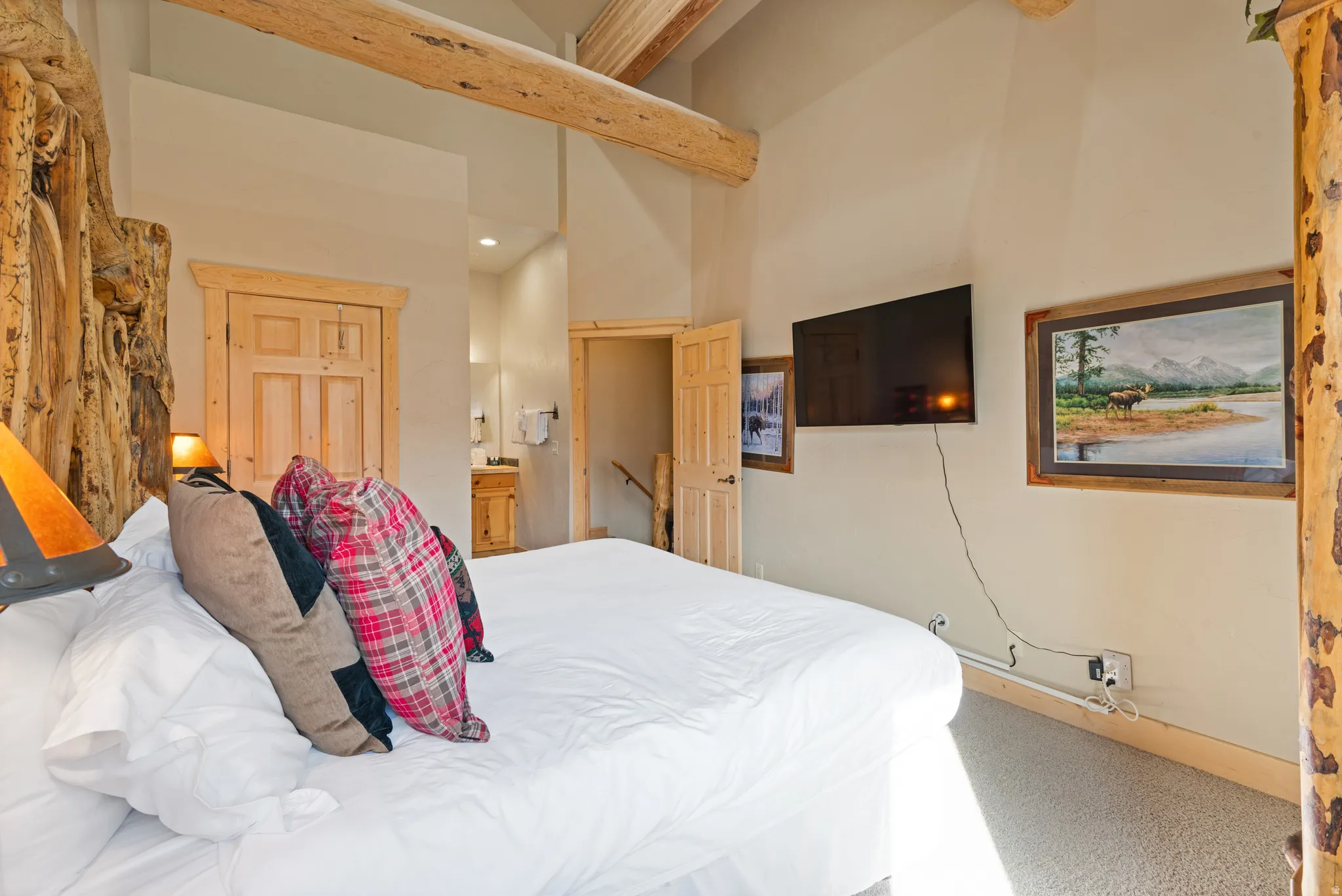 Spacious room featuring vaulted ceilings with exposed wood beams, a built-in entertainment area with a wall-mounted television, and wood-trimmed doorways
