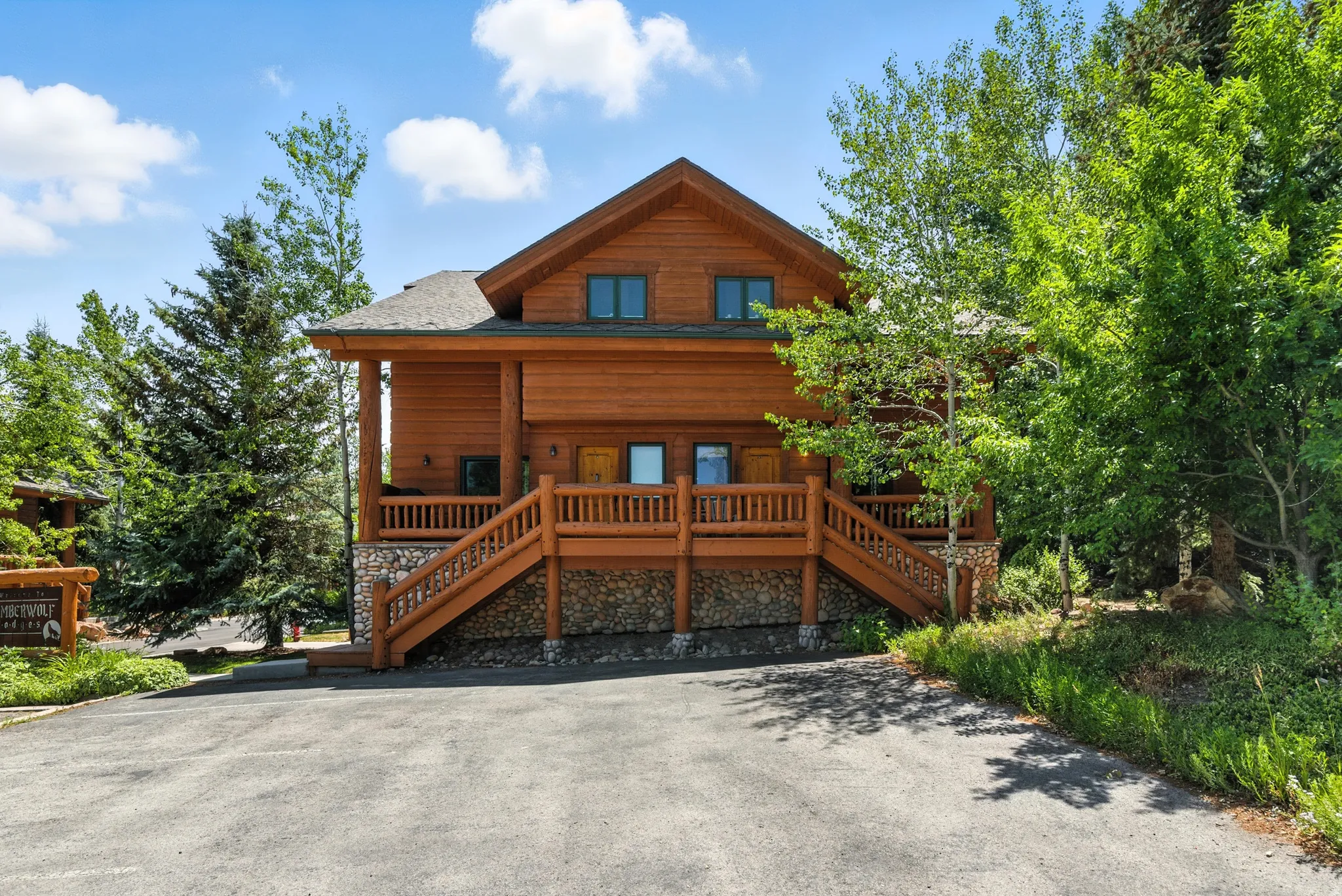 Rustic log cabin residence featuring a stone foundation and a prominent wooden staircase leading to the main entrance