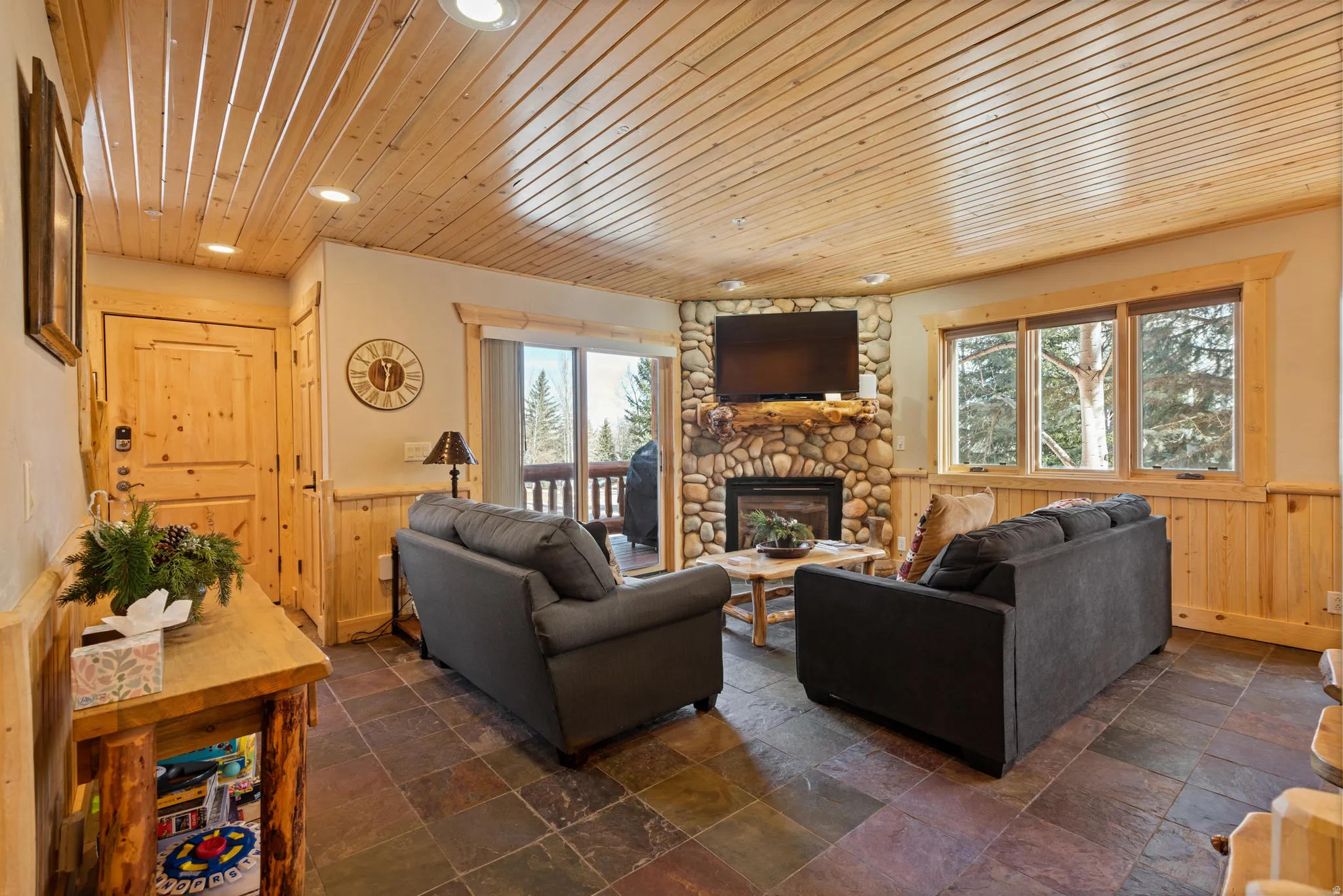 Living area featuring a stone fireplace with a wood-finish mantel, wood-paneled walls, and wood-finish ceilings with recessed lighting