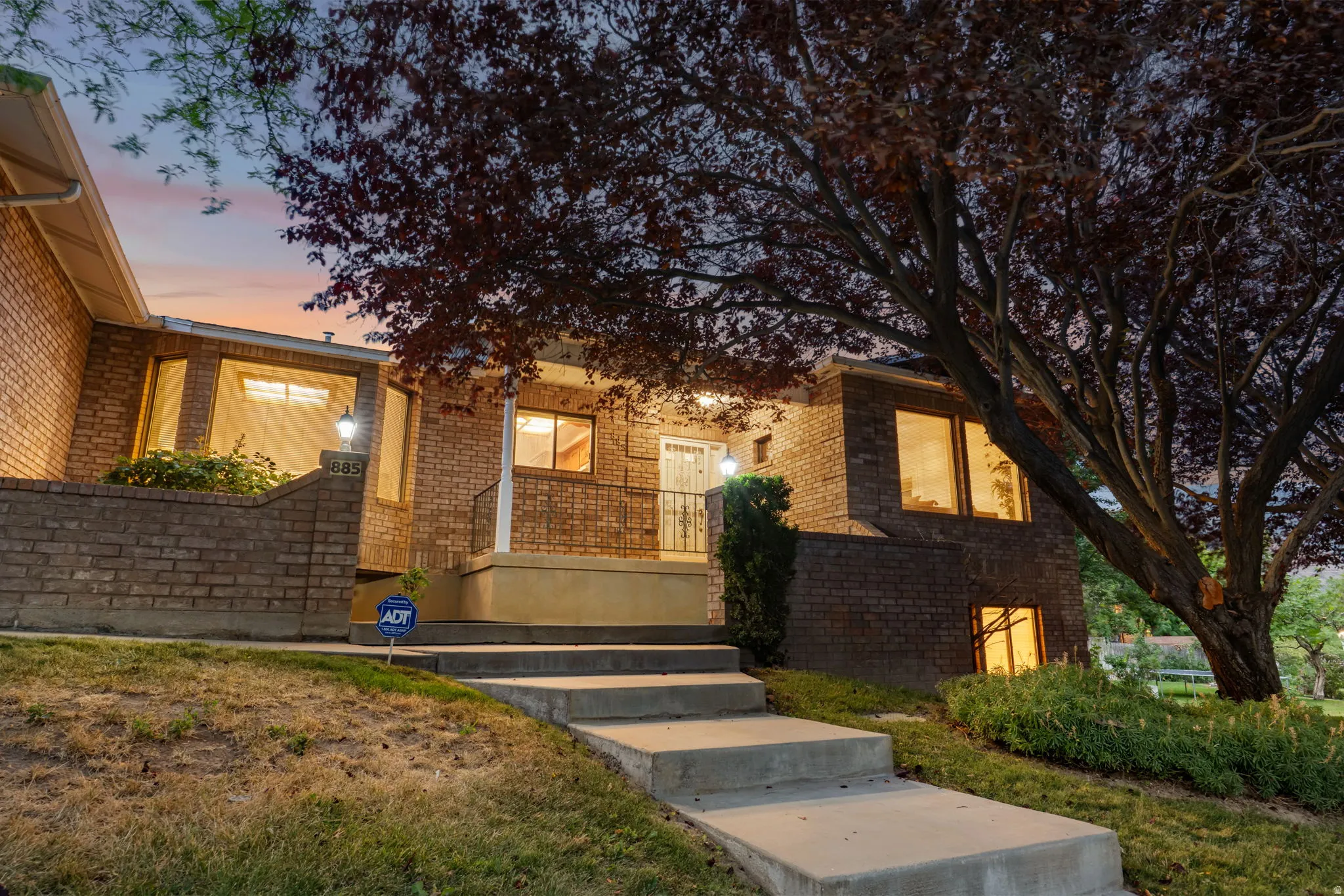 Brick exterior residence featuring a tiered concrete walkway, mature front landscaping, and multiple large windows