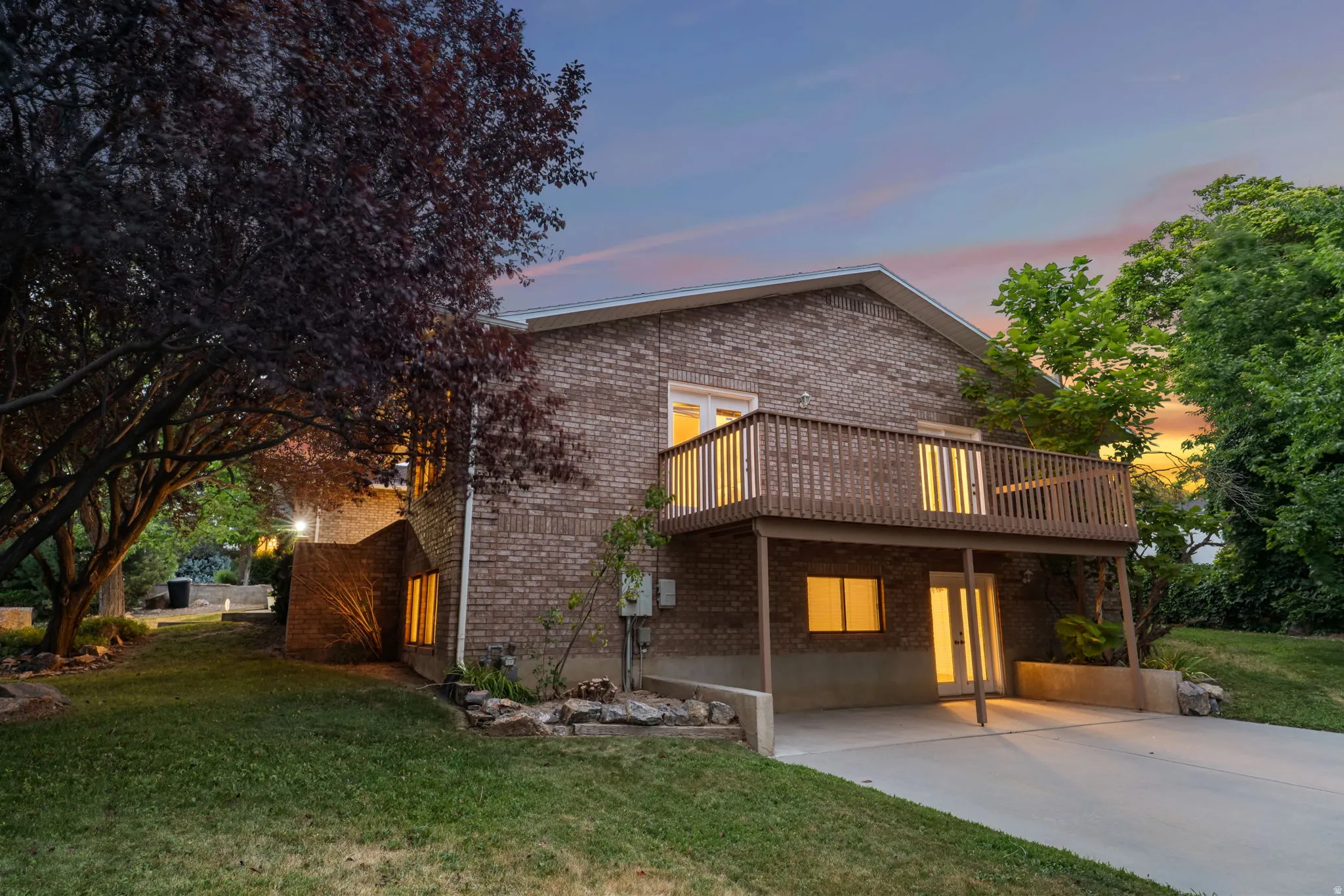 Brick exterior featuring a multi-level structure with a second-story wooden deck and ground-level patio