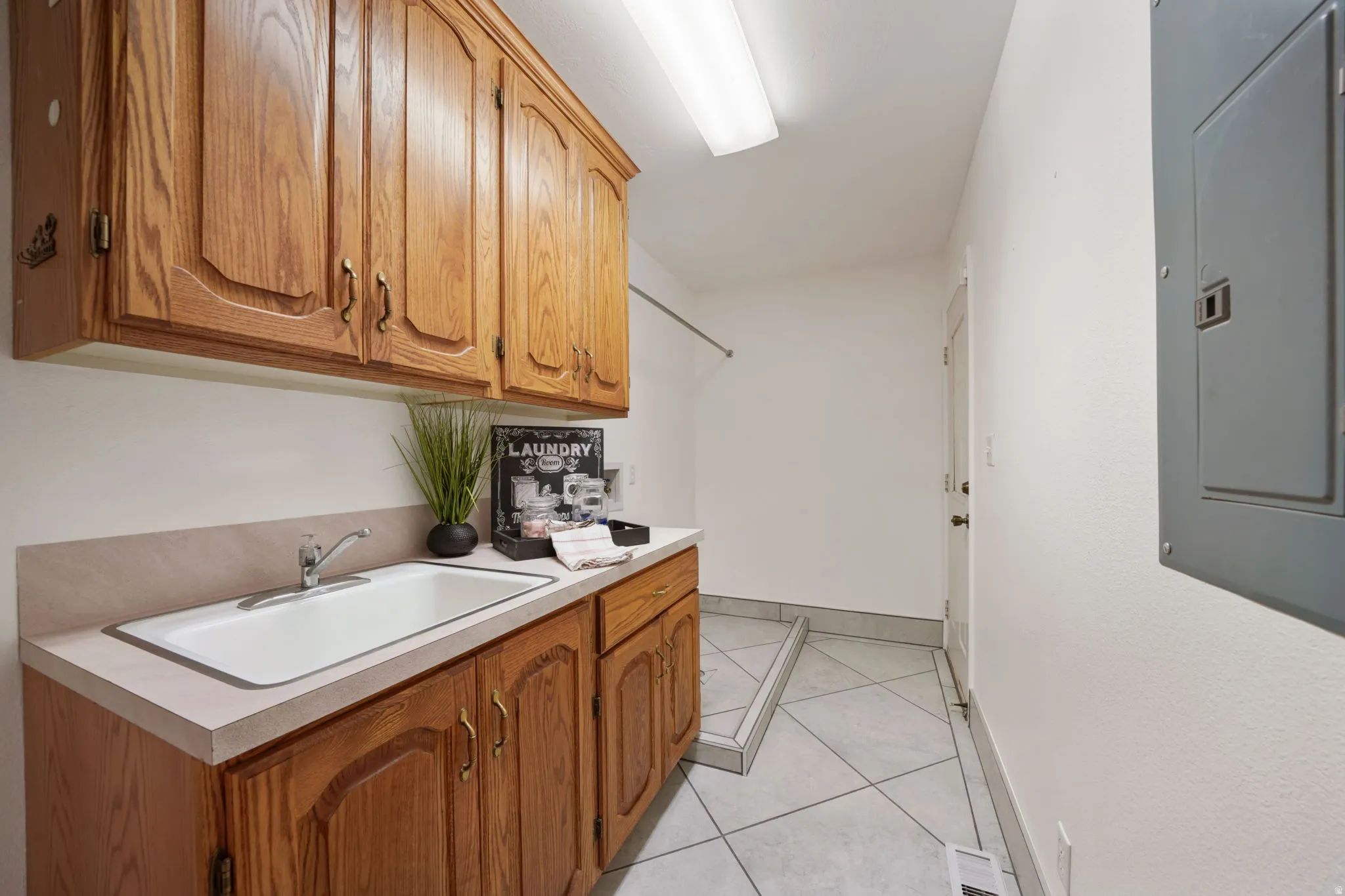 Dedicated utility space featuring ample wood cabinetry, a utility sink with a chrome faucet, light-toned countertops, and tiled flooring