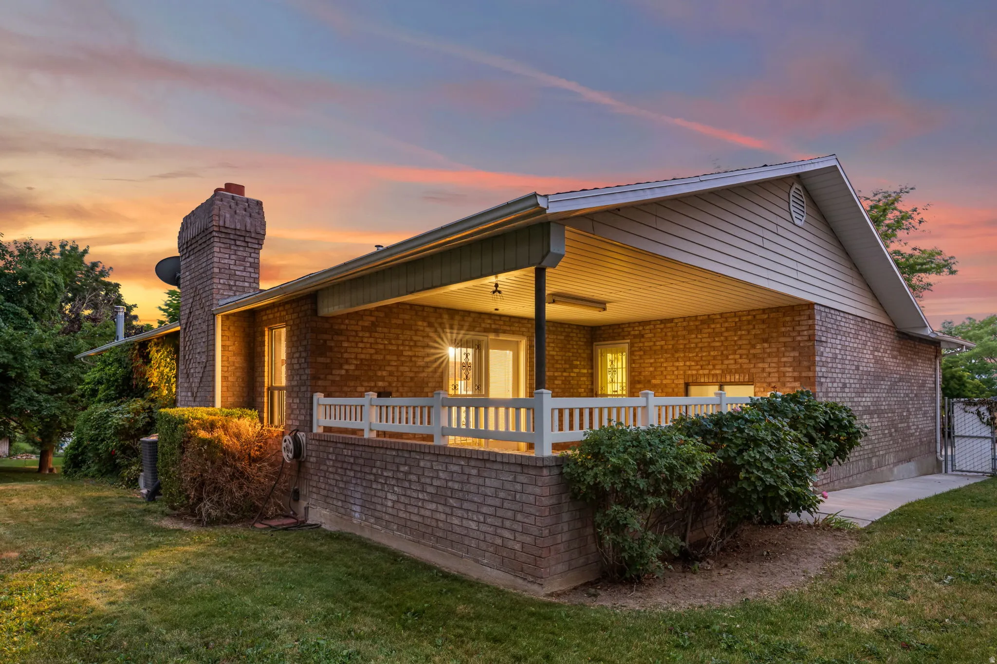 Brick exterior featuring a covered porch with white railing, a prominent brick chimney, and a side-gabled roof with vinyl siding