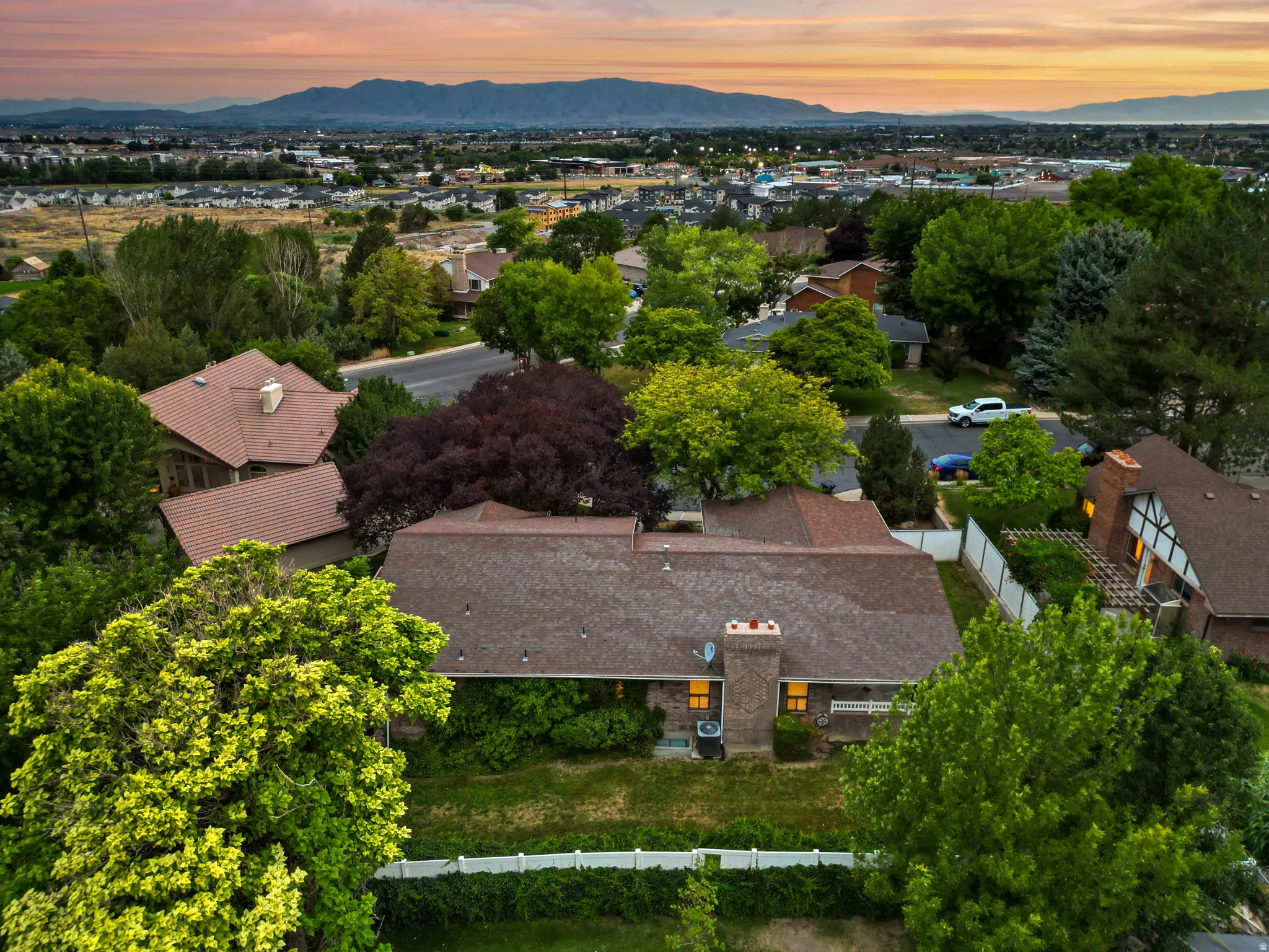 Residential property featuring a shingled roof, brick chimney, and a landscaped yard with mature trees