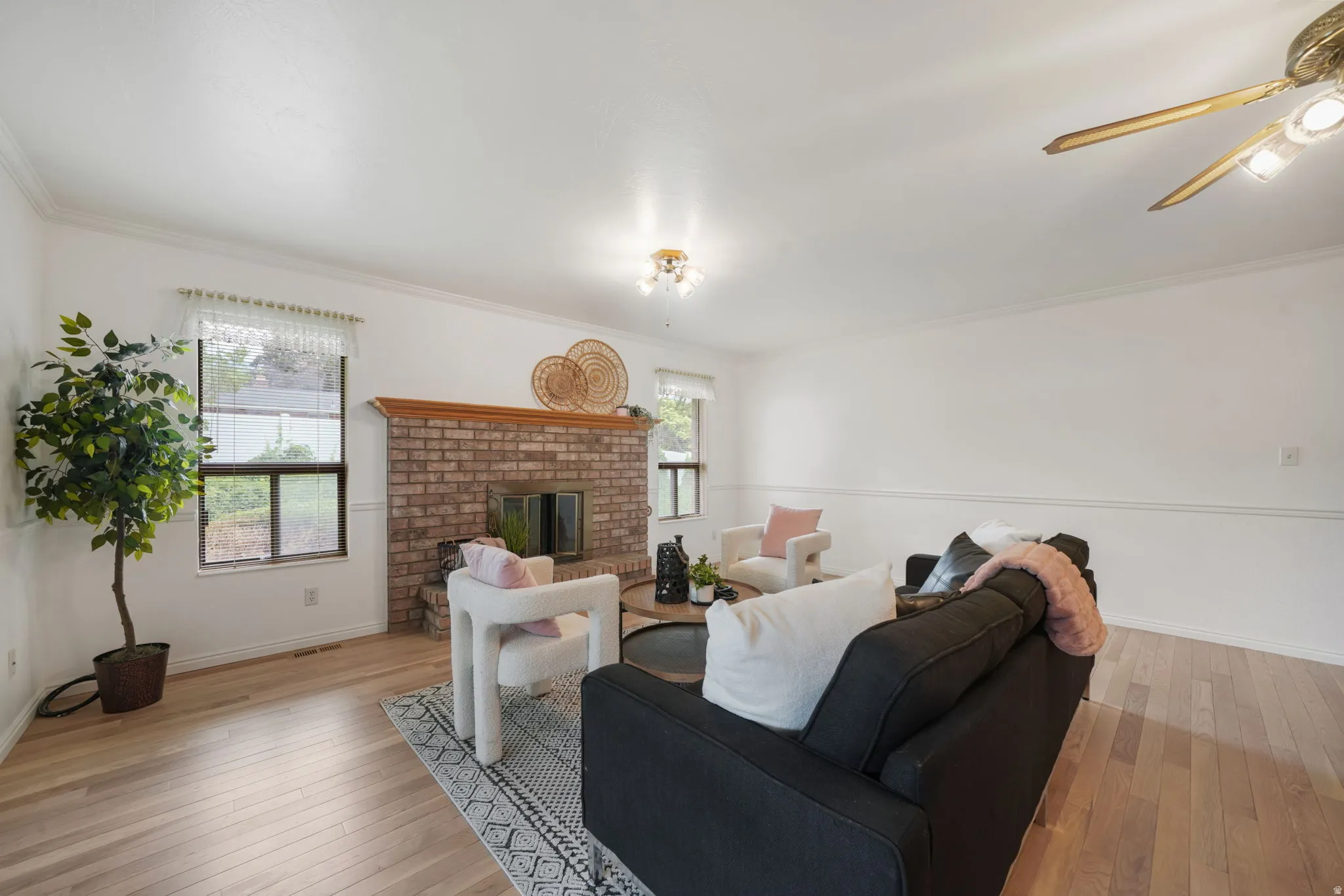 Living area featuring a brick fireplace with a wood mantle, wood-finish flooring, two windows, and crown molding