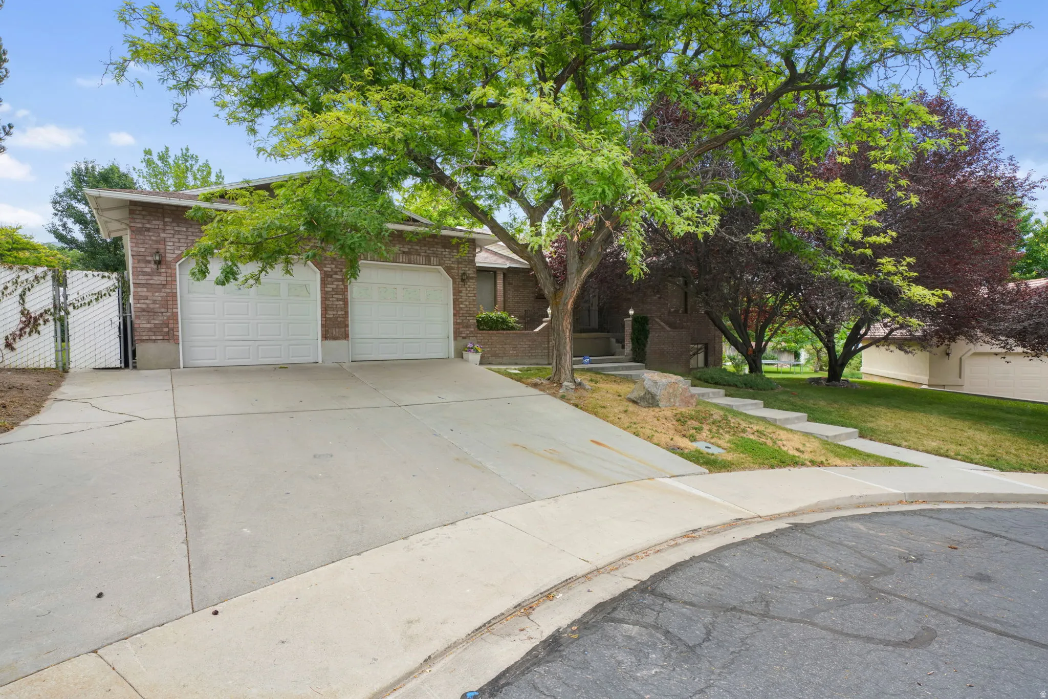 Brick exterior residence featuring a two-car garage with panel doors, a concrete driveway, and established front yard trees