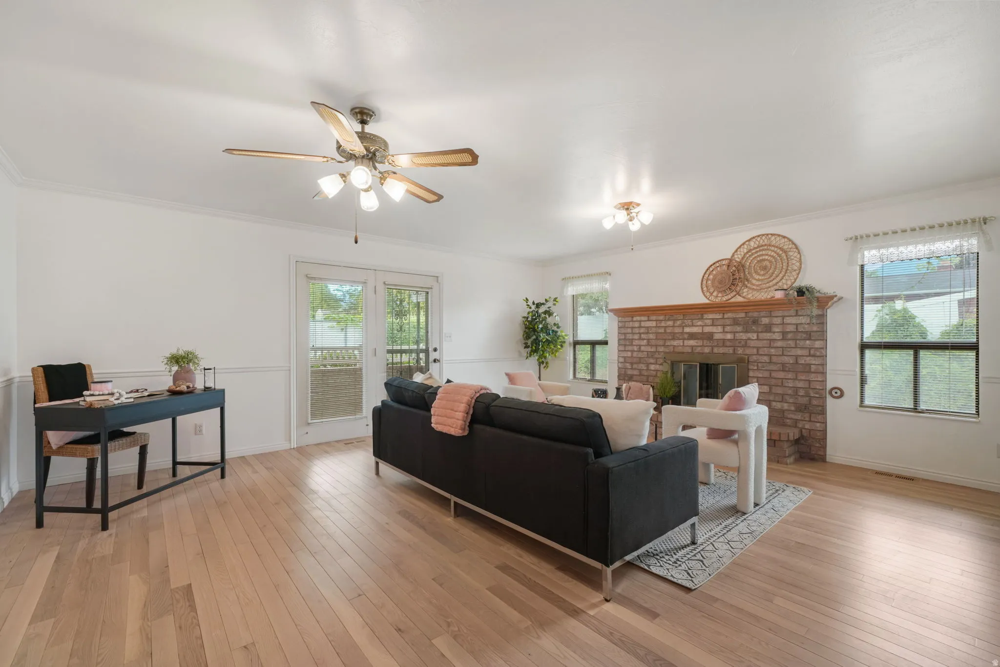 Spacious living area featuring light wood-finish flooring, a brick fireplace with a wood mantle, and white walls with crown molding