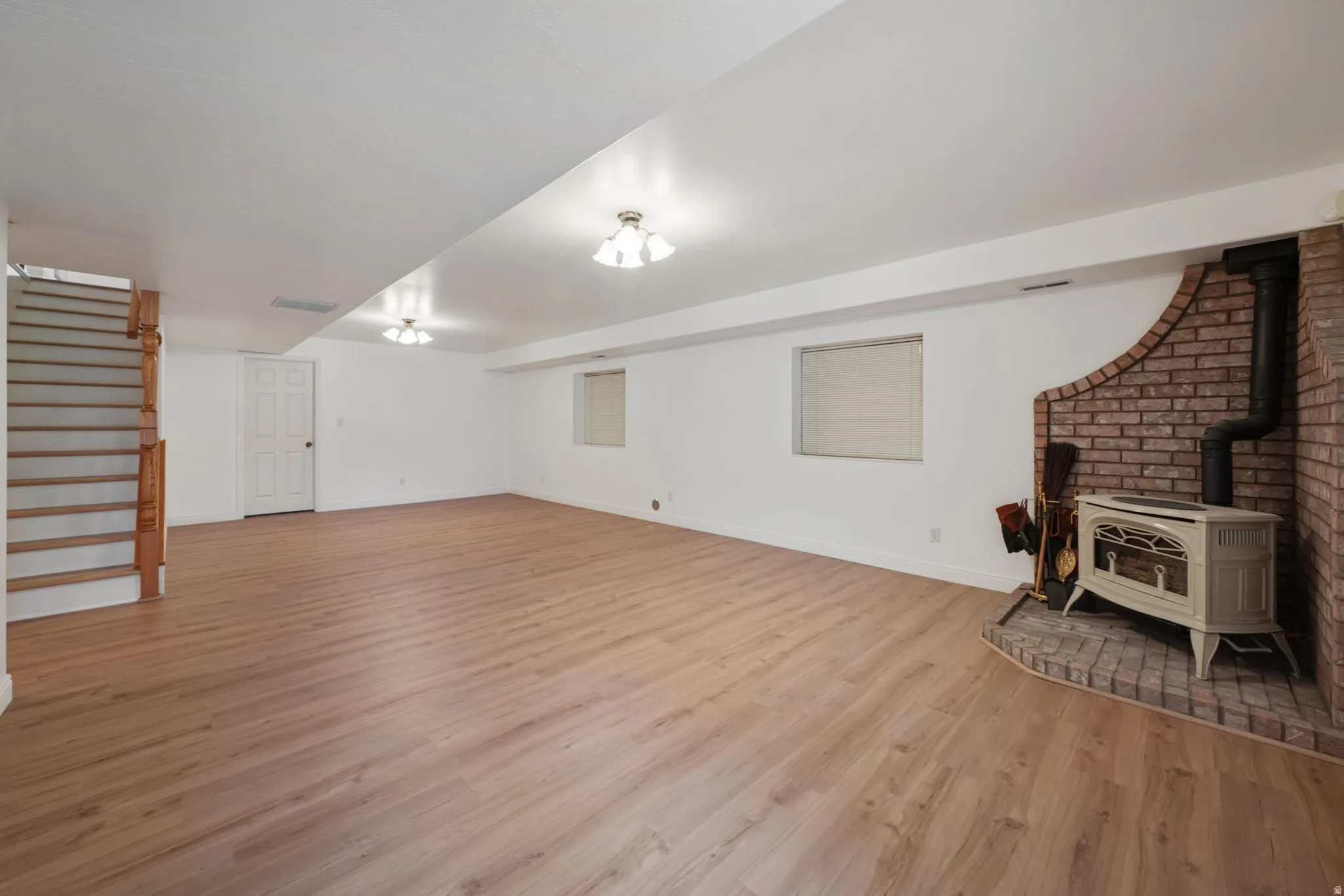 Spacious room featuring wood-finish flooring, a brick-surround wood-burning stove, and recessed lighting