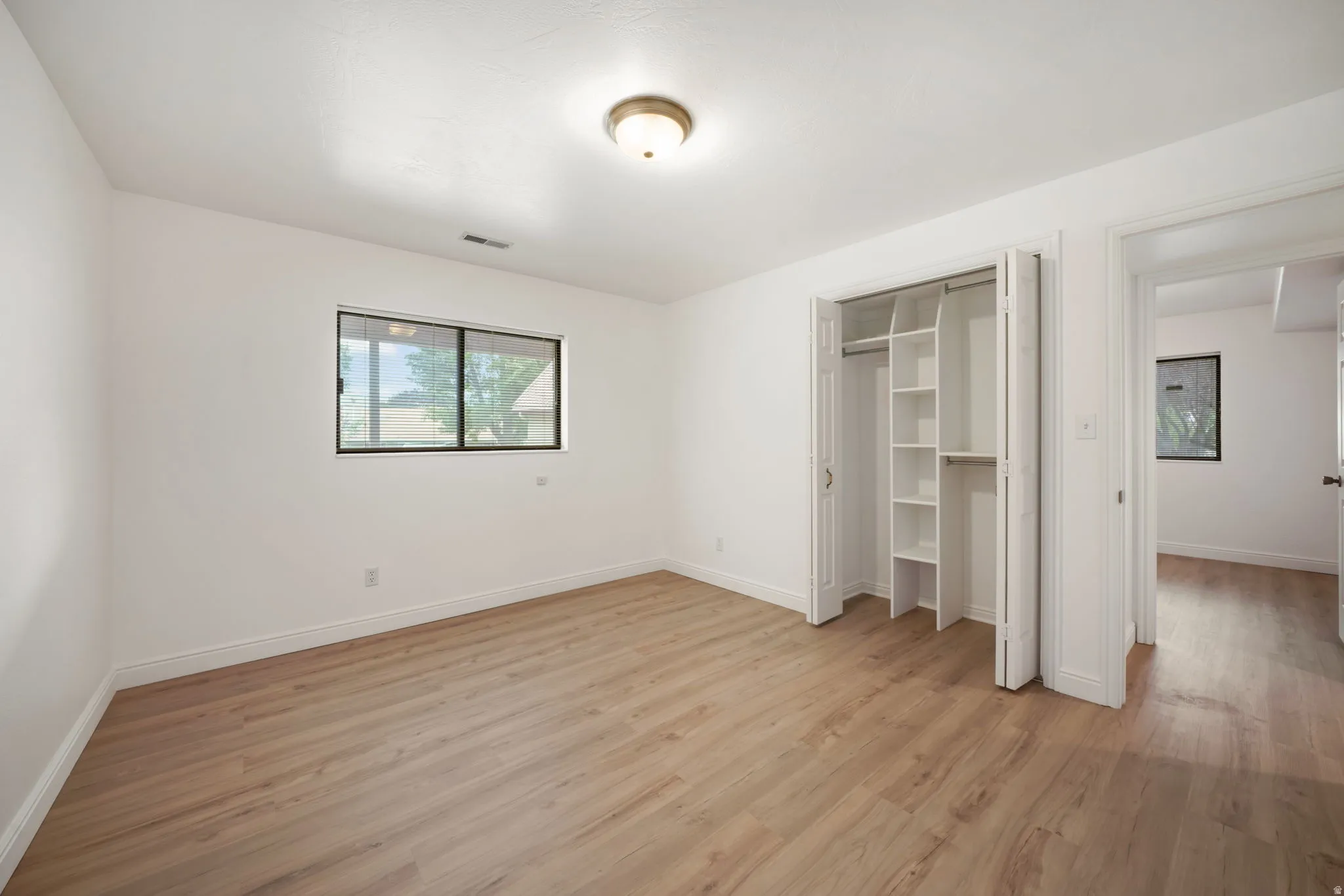 Bright room featuring wood-finish flooring, white walls, and a window with black trim