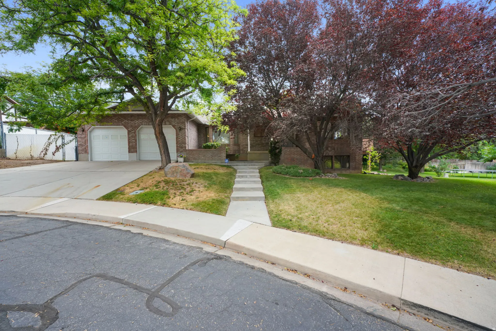 Brick exterior residence featuring a two-car garage, concrete driveway, and mature landscaping