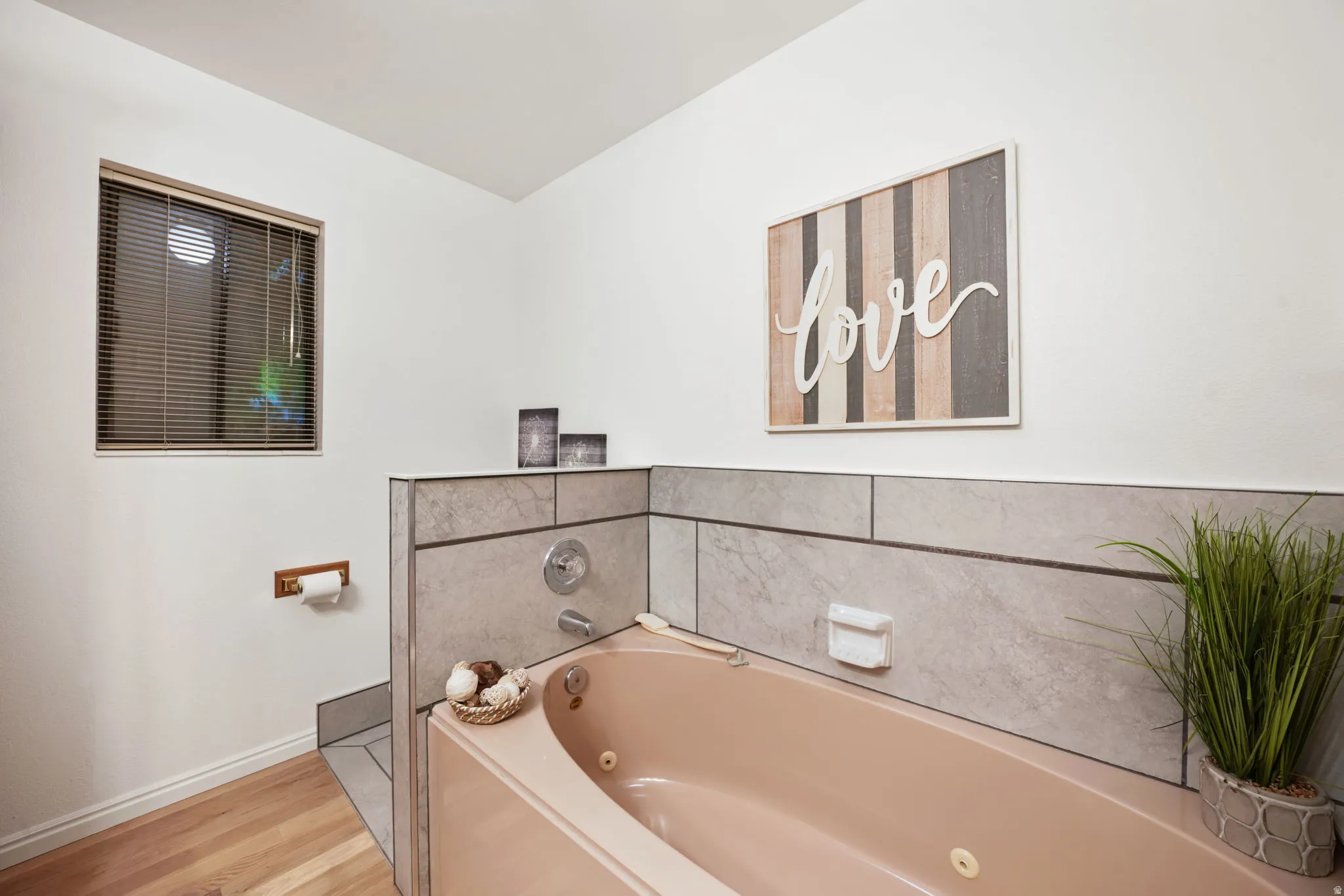 Soaking tub with tile surround, wood-finish flooring, and window with blinds