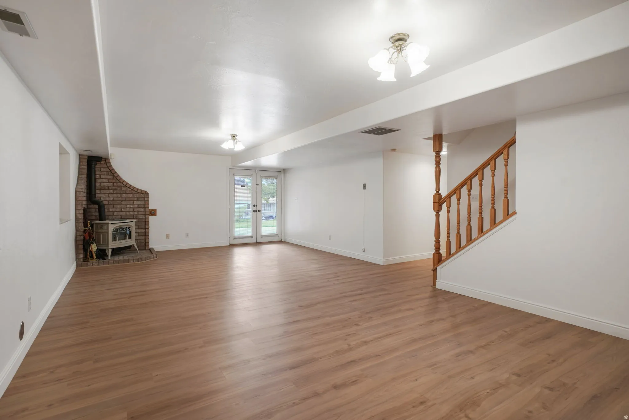Spacious lower-level area featuring wood-finish flooring, a brick-surround wood stove, and a white French door