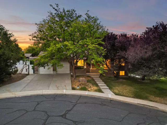 Brick facade residence featuring a two-car garage, mature landscaping, concrete driveway, and a paved walkway leading to the entrance