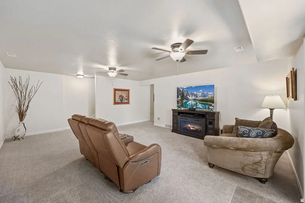Spacious living area featuring light gray carpeting, neutral wall colors, and multiple ceiling fans for circulation