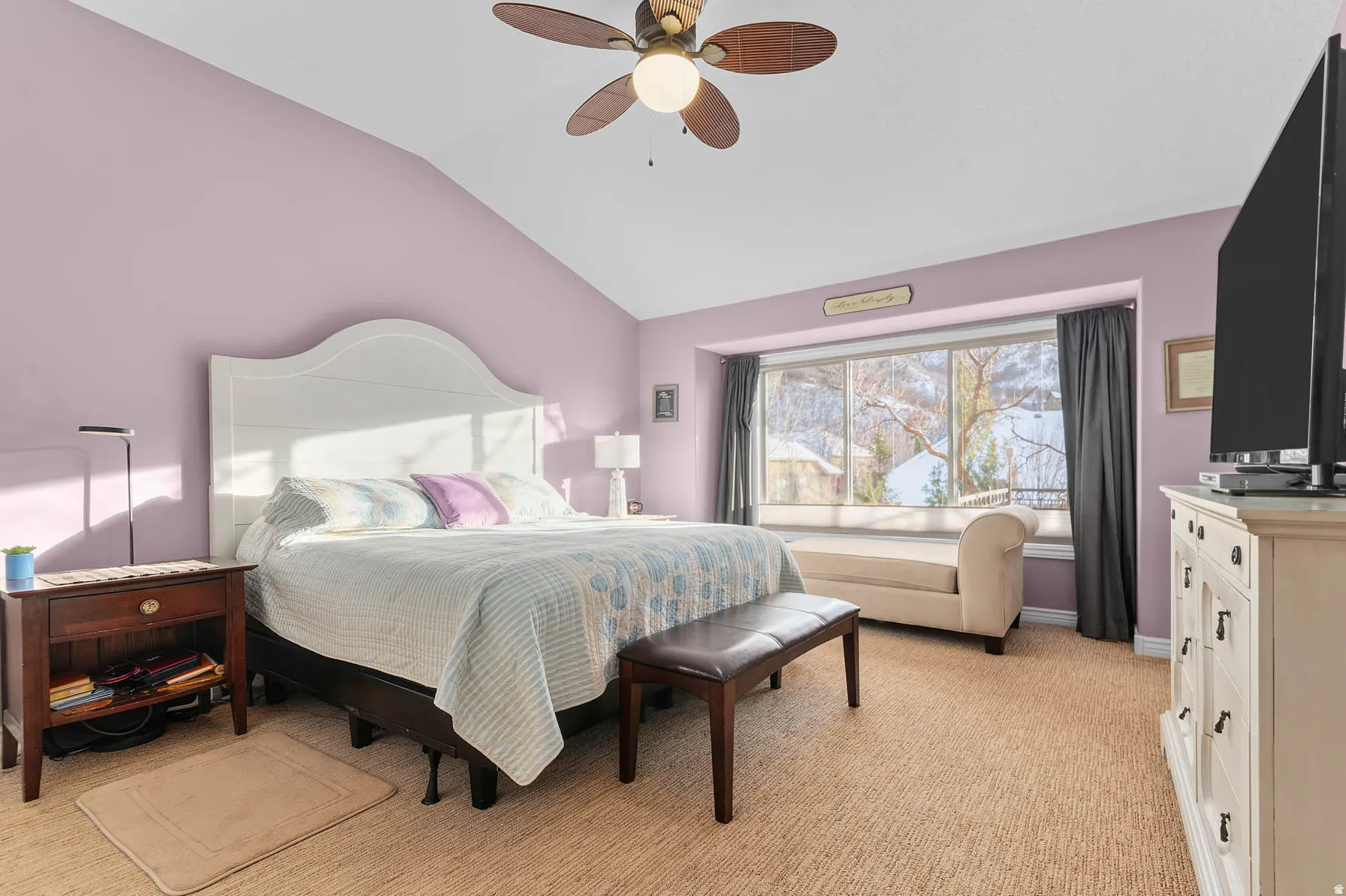 Vaulted ceiling bedroom with a ceiling fan, broad window, and neutral-toned carpeting