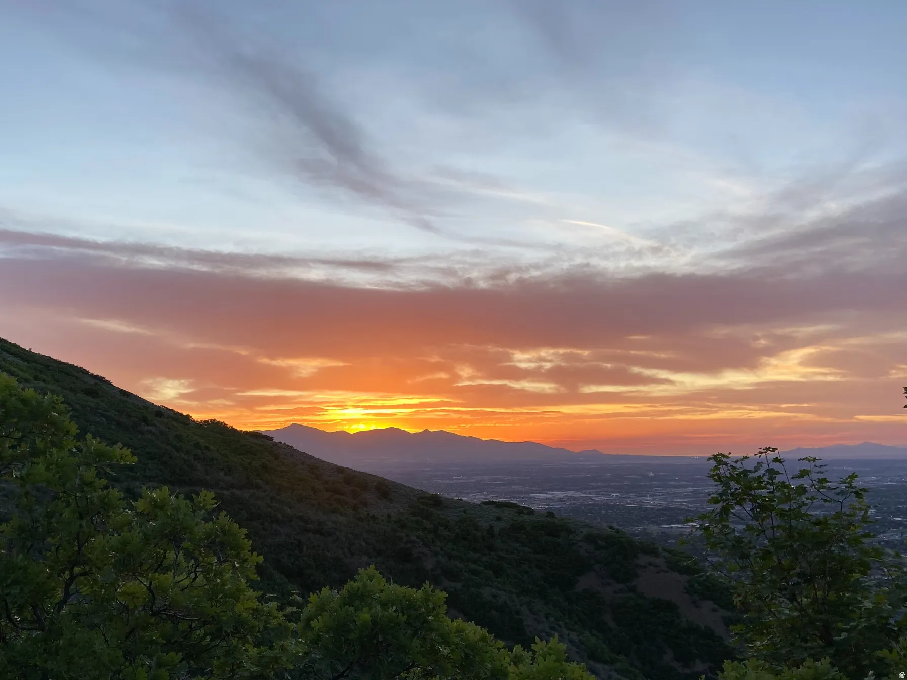 Expansive mountain scenery with a vibrant sunset and distant city lights