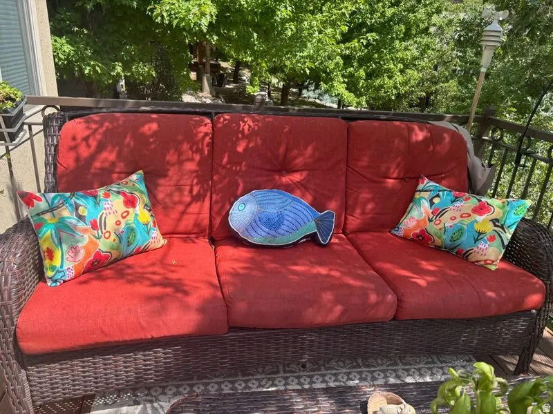 Woven outdoor sofa with red cushions and a dark-toned railing, set against a backdrop of lush green foliage