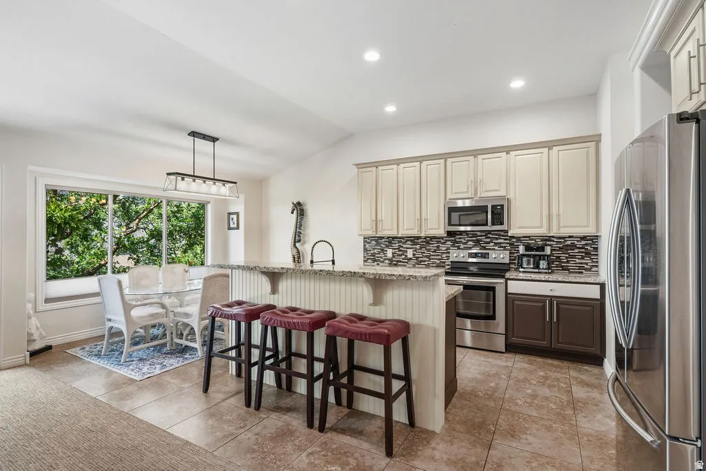 Kitchen featuring a multi-tone tile backsplash, stainless steel appliances, and a breakfast bar with a granite-look countertop