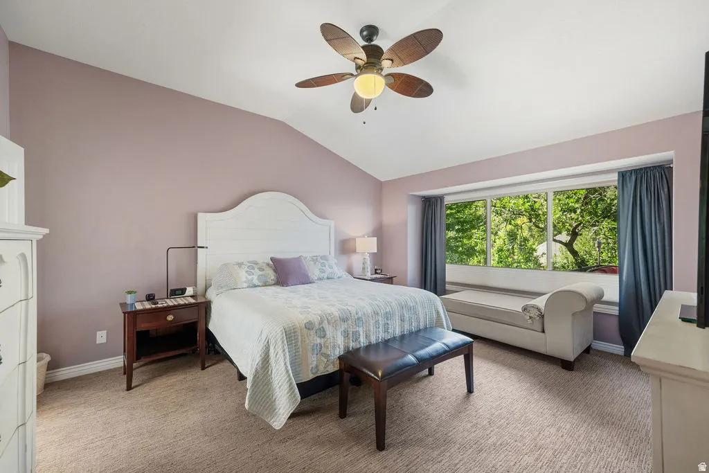 Vaulted ceiling bedroom featuring a white shiplap headboard, recessed window seating, large picture windows, and a ceiling fan with integrated lighting